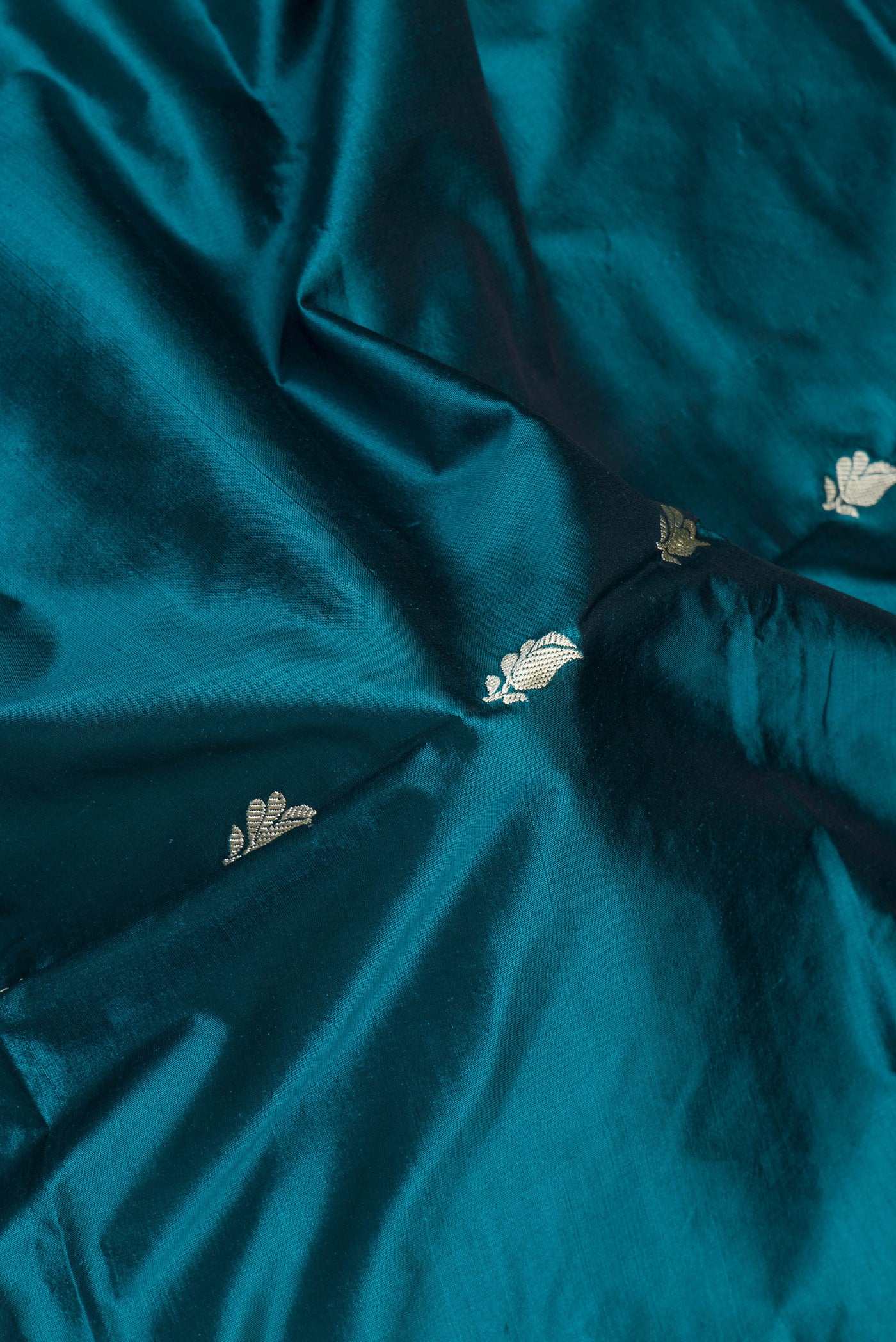 Close up of Peacock Blue Dual Tone Banarasi Silk Saree with Thread Butta on the body and Thread Border.  displaying folds