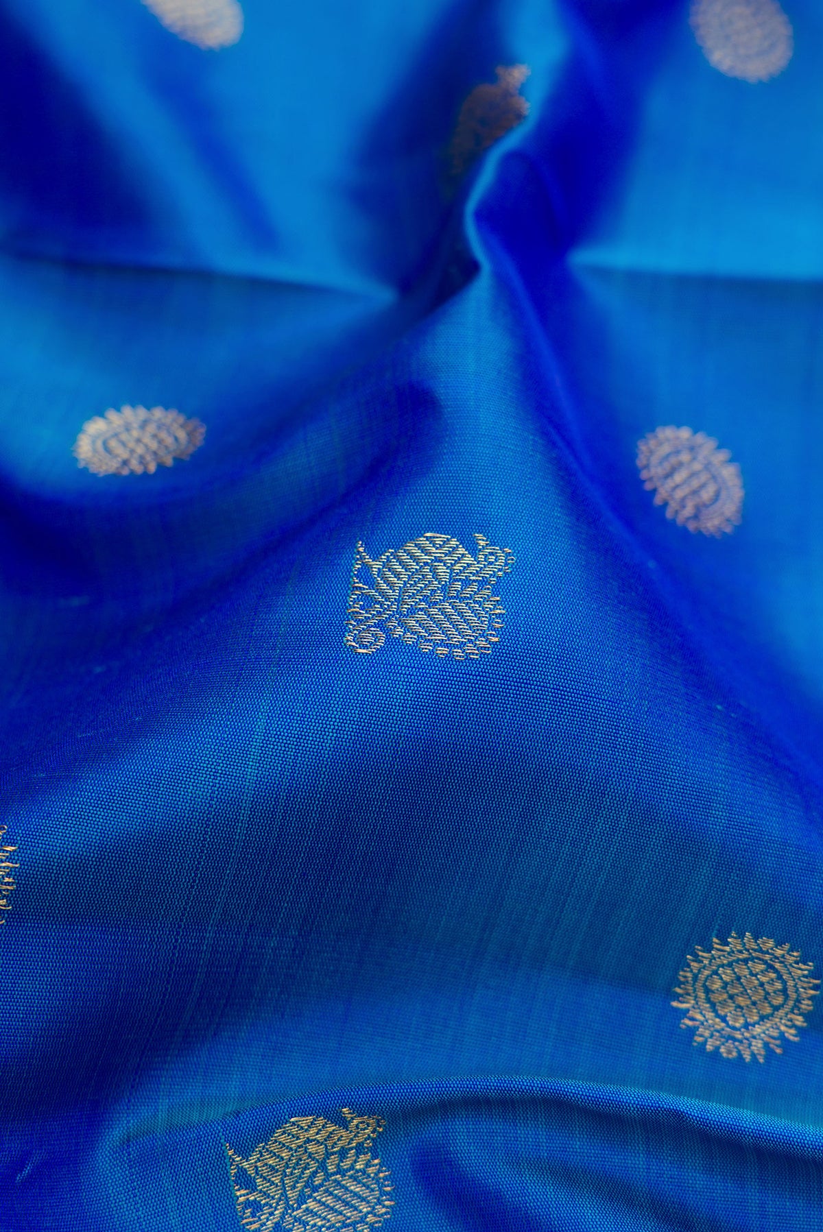 Close up of Pure Silk Pure Zari Peacock Blue Dual Tone Kanjivaram Saree with Zari Butta on the body and Zari Border.  displaying folds