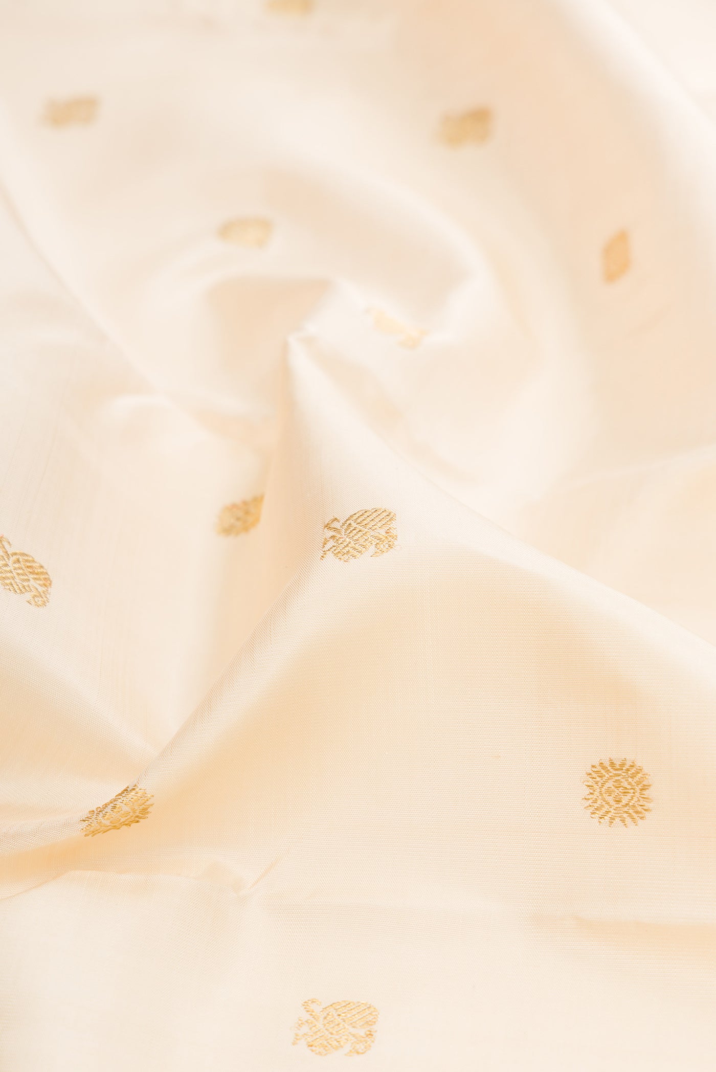 Close up of Pure Silk Pure Zari Cream Kanjivaram Saree with Zari Butta on the body and Fancy Border.  displaying folds