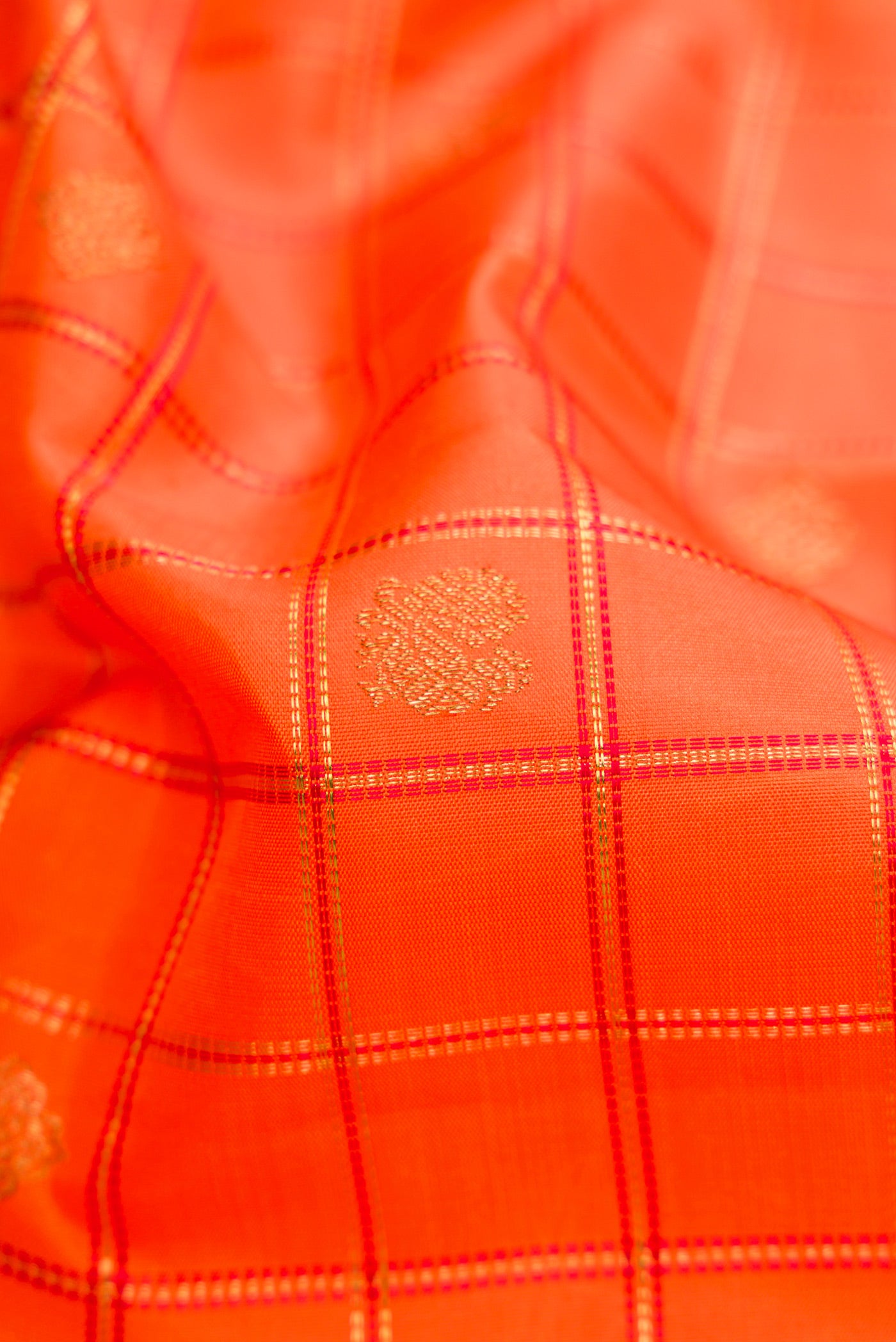 Close up of Pure Silk Pure Zari Orange Dual Tone Kanchipuram Saree with Checked design on the body and Zari Border.  displaying folds