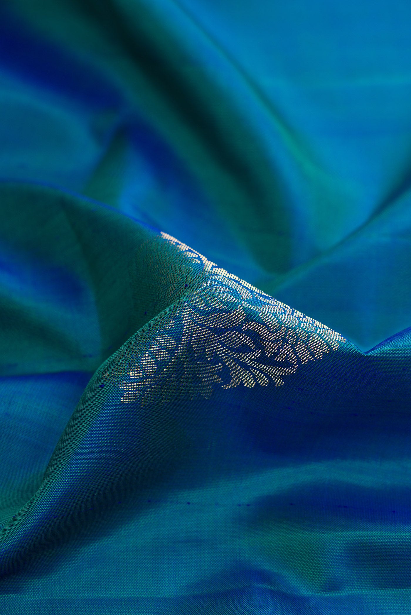 Close up of Peacock Blue Dual Tone Soft Silk Saree with Zari Butta on the body and Zari Border.  displaying folds
