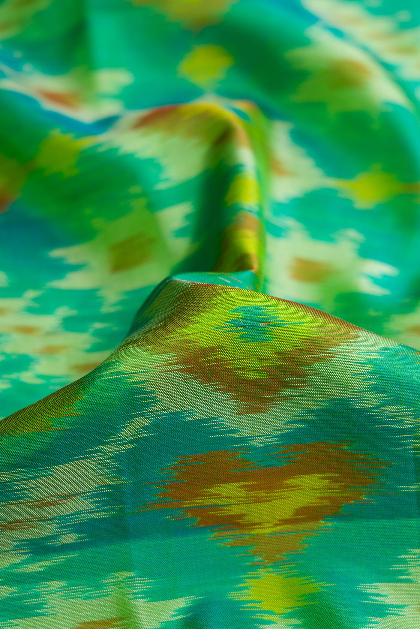 Close up of Green Dual Tone Soft Silk Saree with Ikat Print on the body and Zari Border.  displaying folds