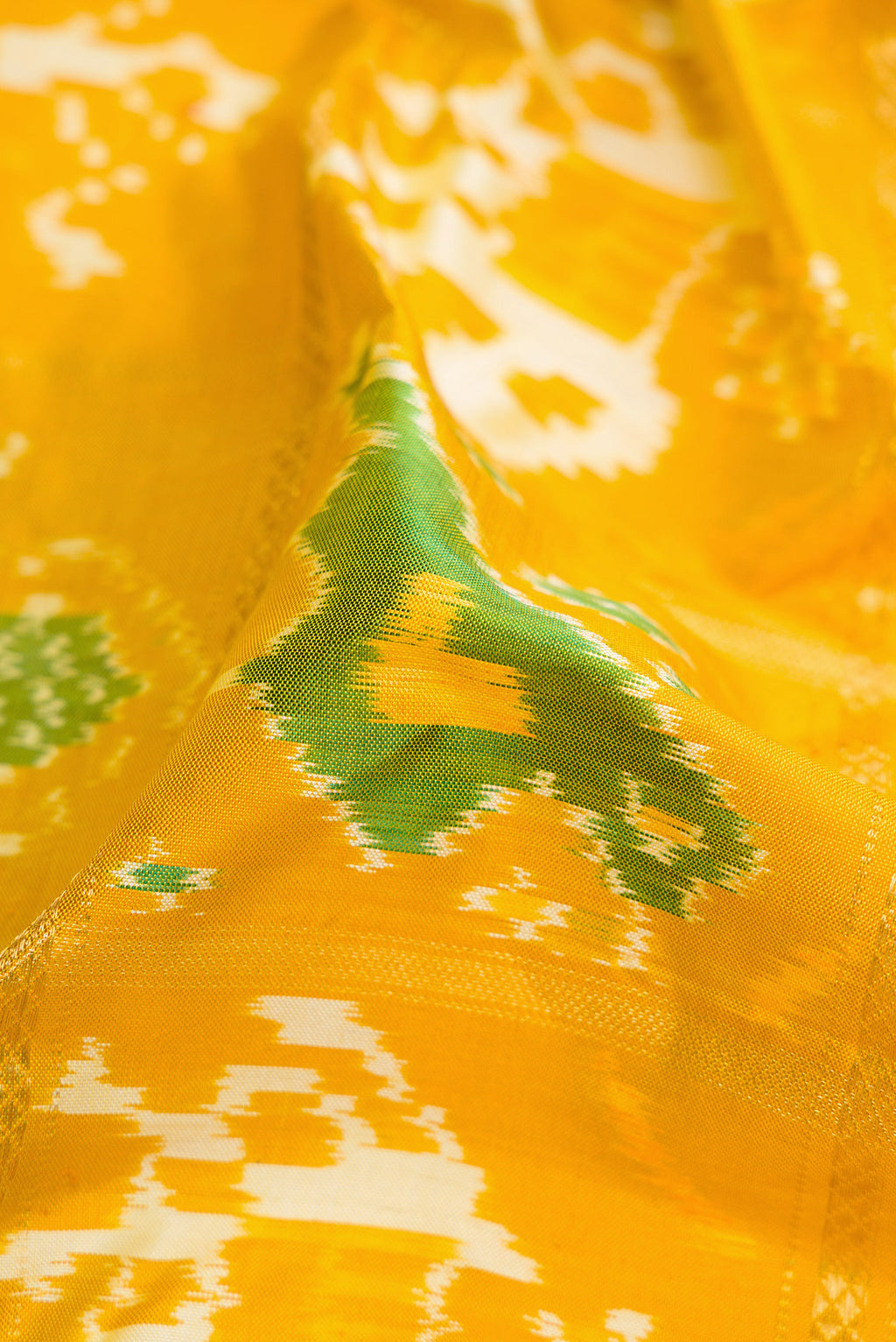Close up of Mustard Dual Tone Double Ikat Saree with Ikat Print on the body and Zari Border.  displaying folds