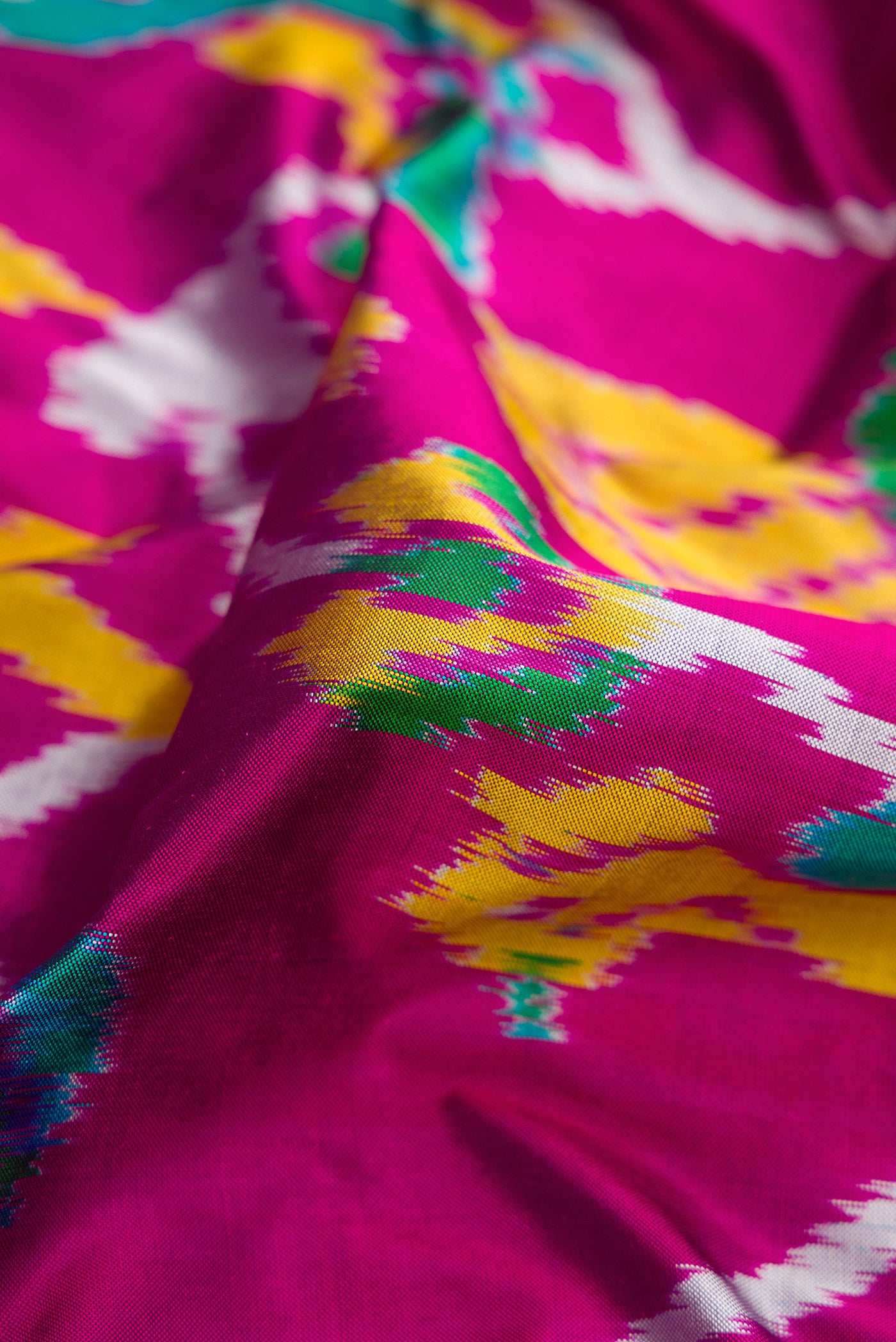 Close up of Magenta Dual Tone Double Ikat Saree with Ikat Print on the body and Ikat Border.  displaying folds