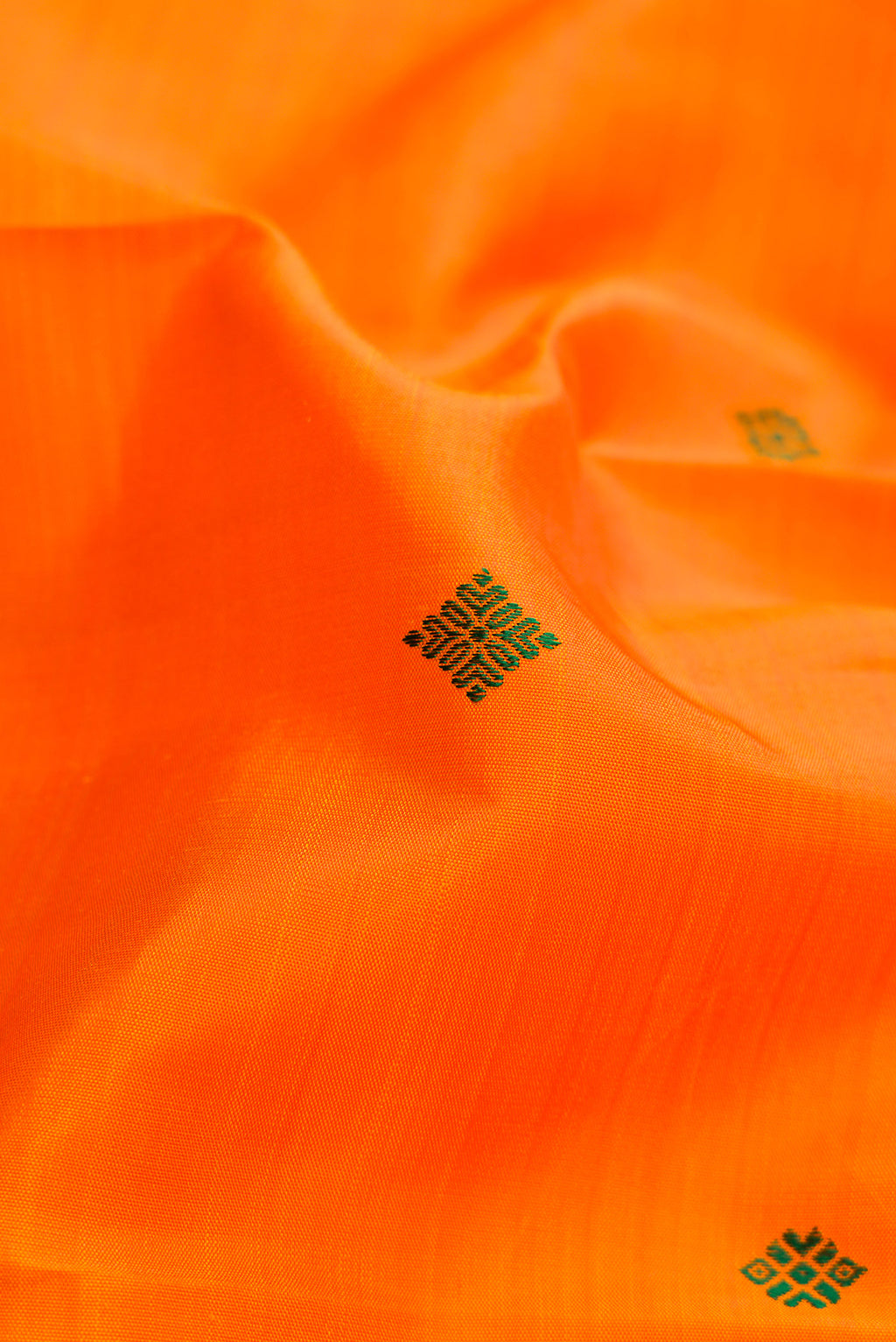 Close up of Pure Silk Pure Zari Orange Dual Tone Kanchipuram Saree with Thread Butta on the body and Zari Border.  displaying folds