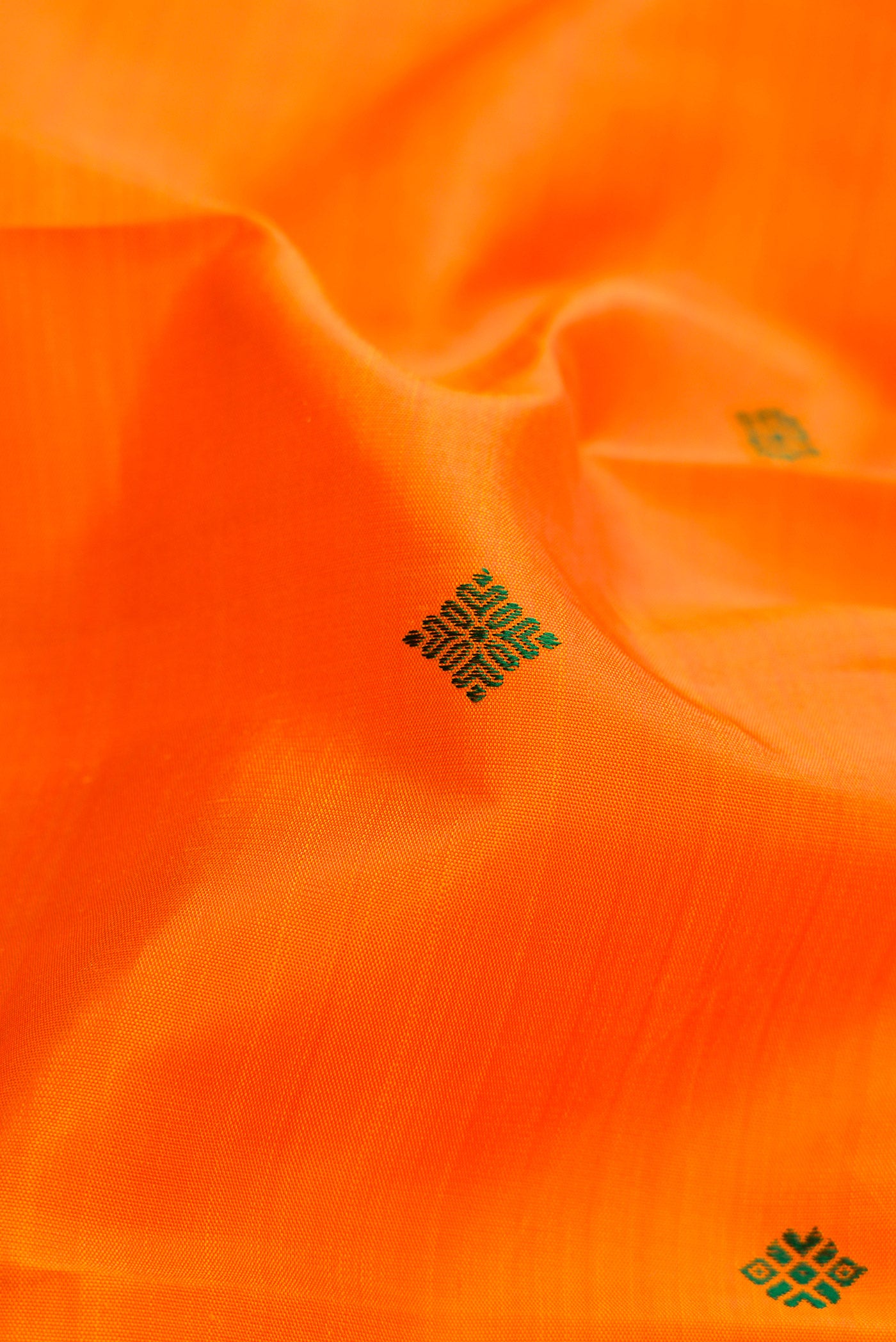 Close up of Pure Silk Pure Zari Orange Dual Tone Kanchipuram Saree with Thread Butta on the body and Zari Border.  displaying folds