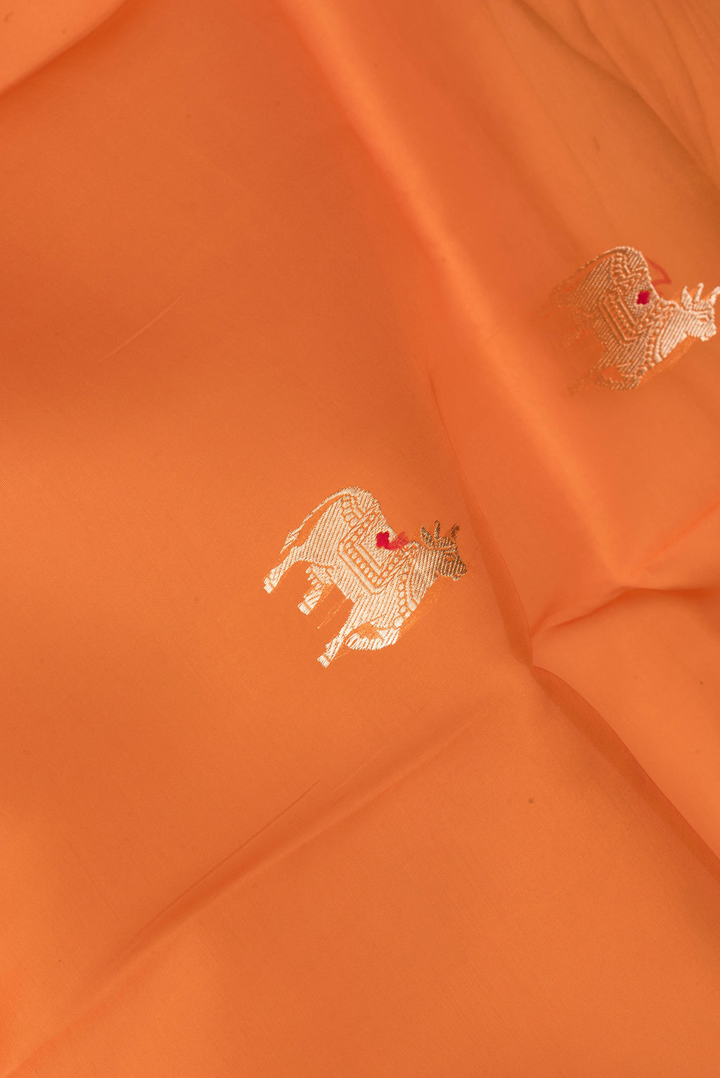 Close up of Orange Organza Silk Saree with Zari Butta on the body and Zari Border.  displaying folds