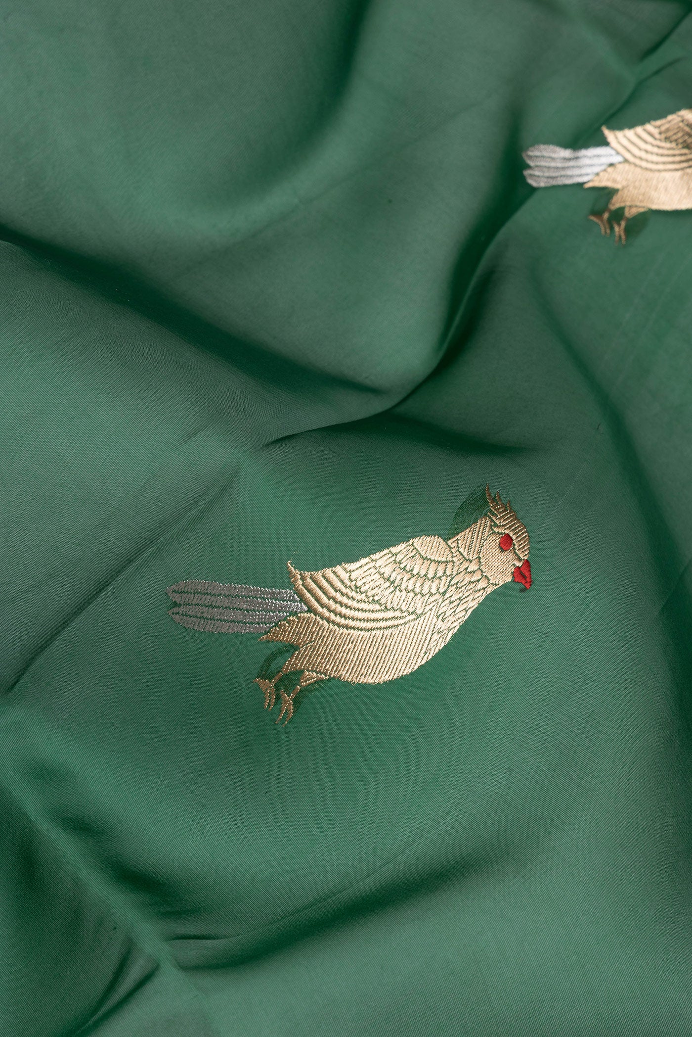 Close up of Bottle Green Organza Silk Saree with Zari And Thread Butta on the body and Zari Border.  displaying folds