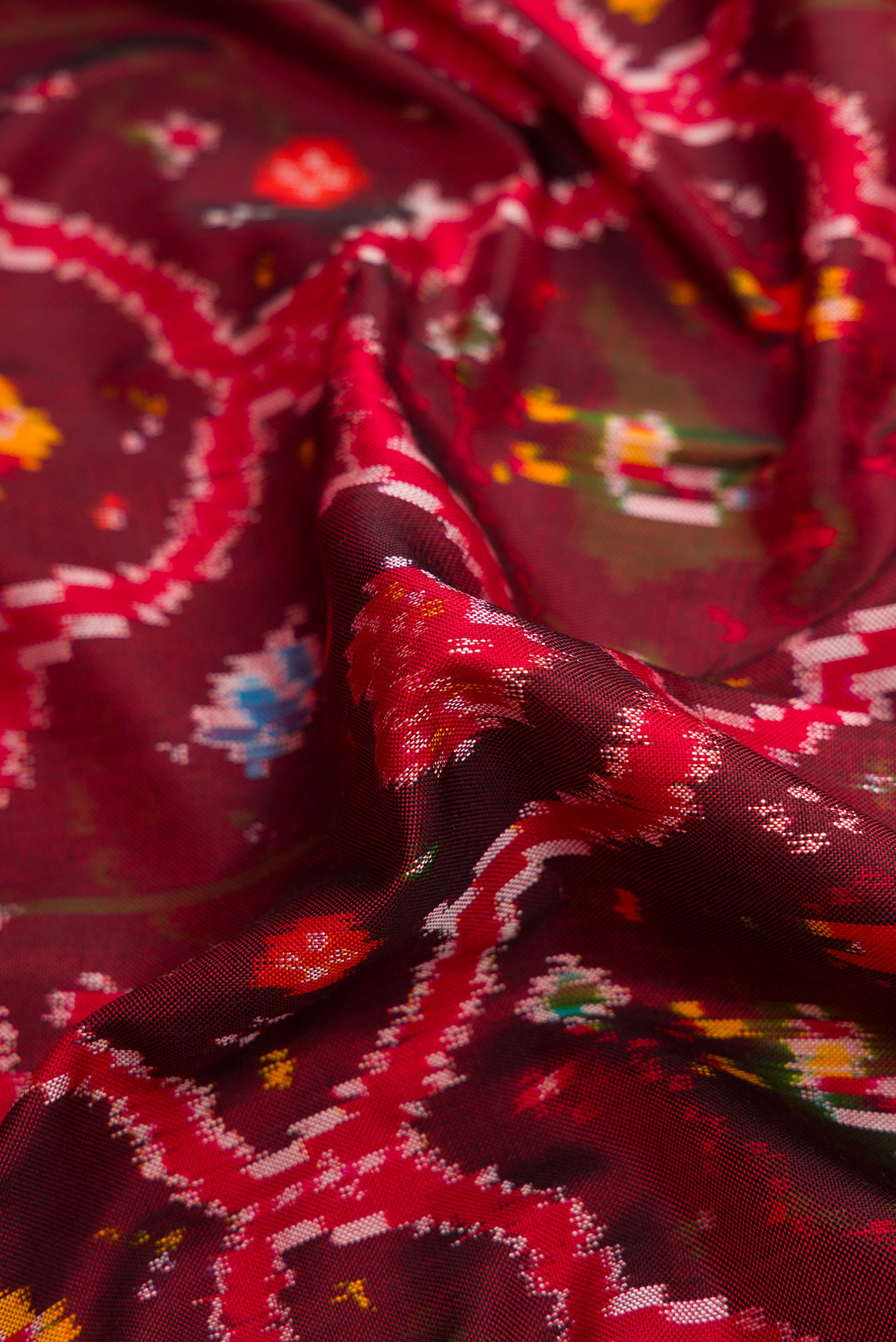 Close up of Maroon Dual Tone Double Ikat Saree with Ikat Print on the body and Zari Border.  displaying folds