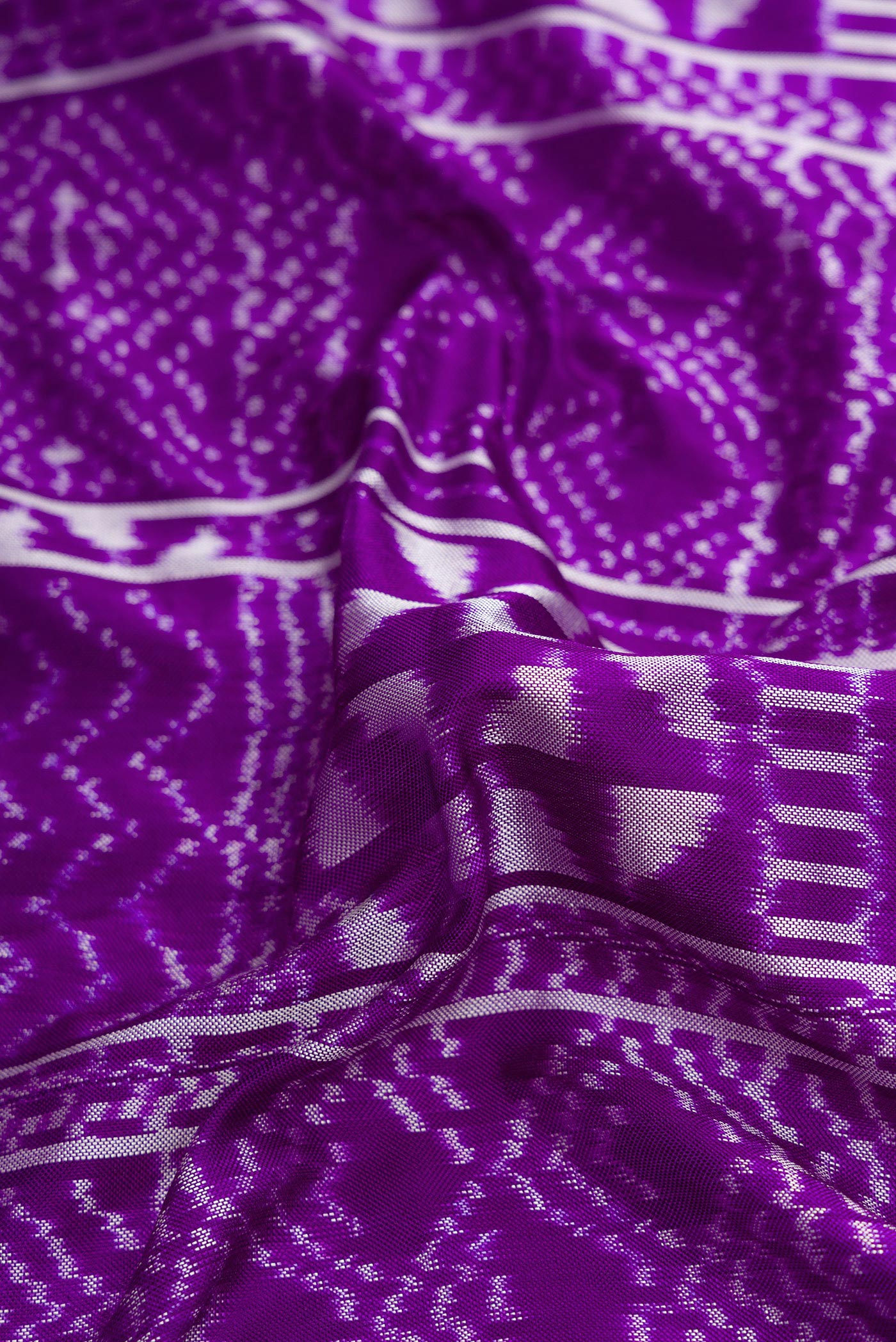 Close up of Violet Dual Tone Double Ikat Saree with Ikat Print on the body and Plain Border.  displaying folds