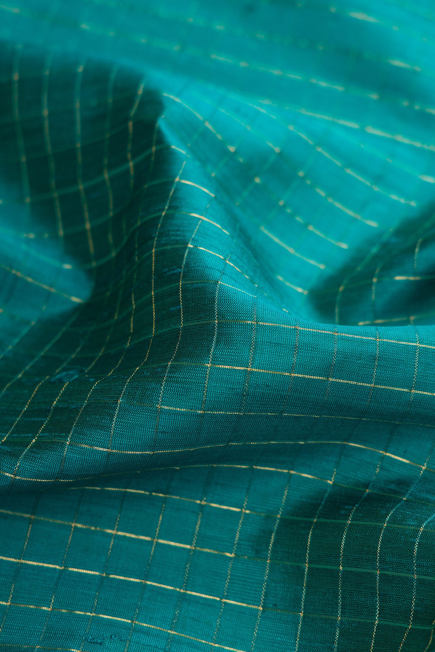 Close up of Peacock Blue Raw Silk Saree with Checked design on the body and Zari Border.  displaying folds