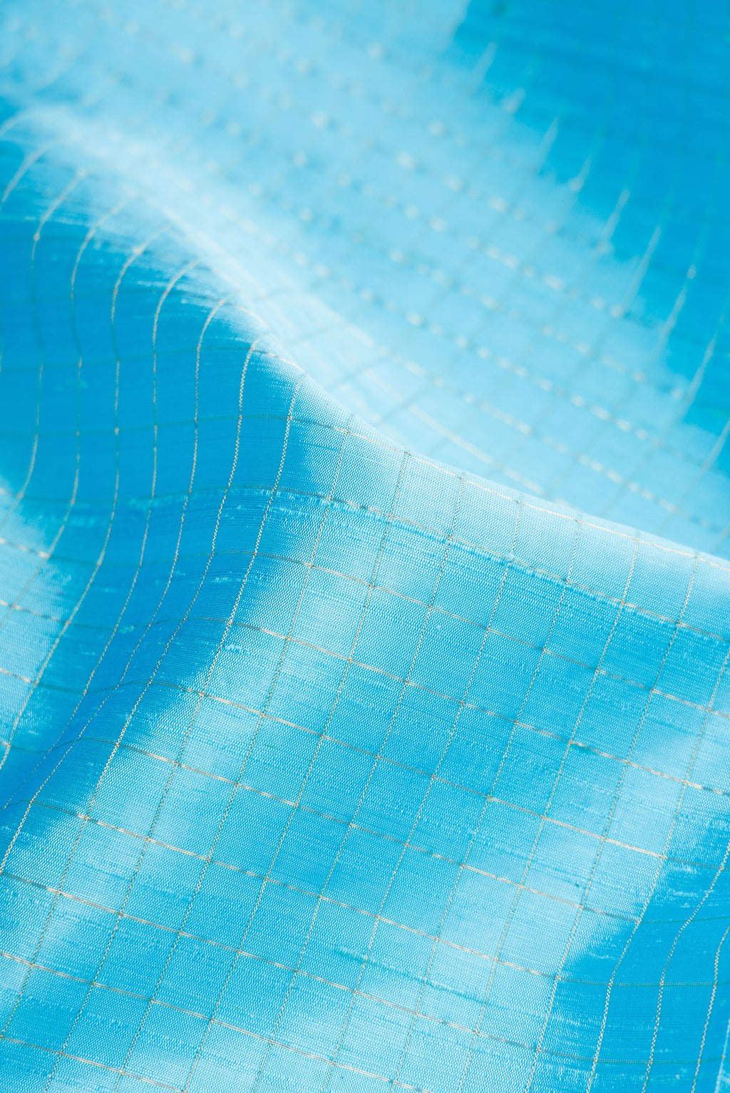 Close up of Sky Blue Raw Silk Saree with Checked design on the body and Zari Border.  displaying folds