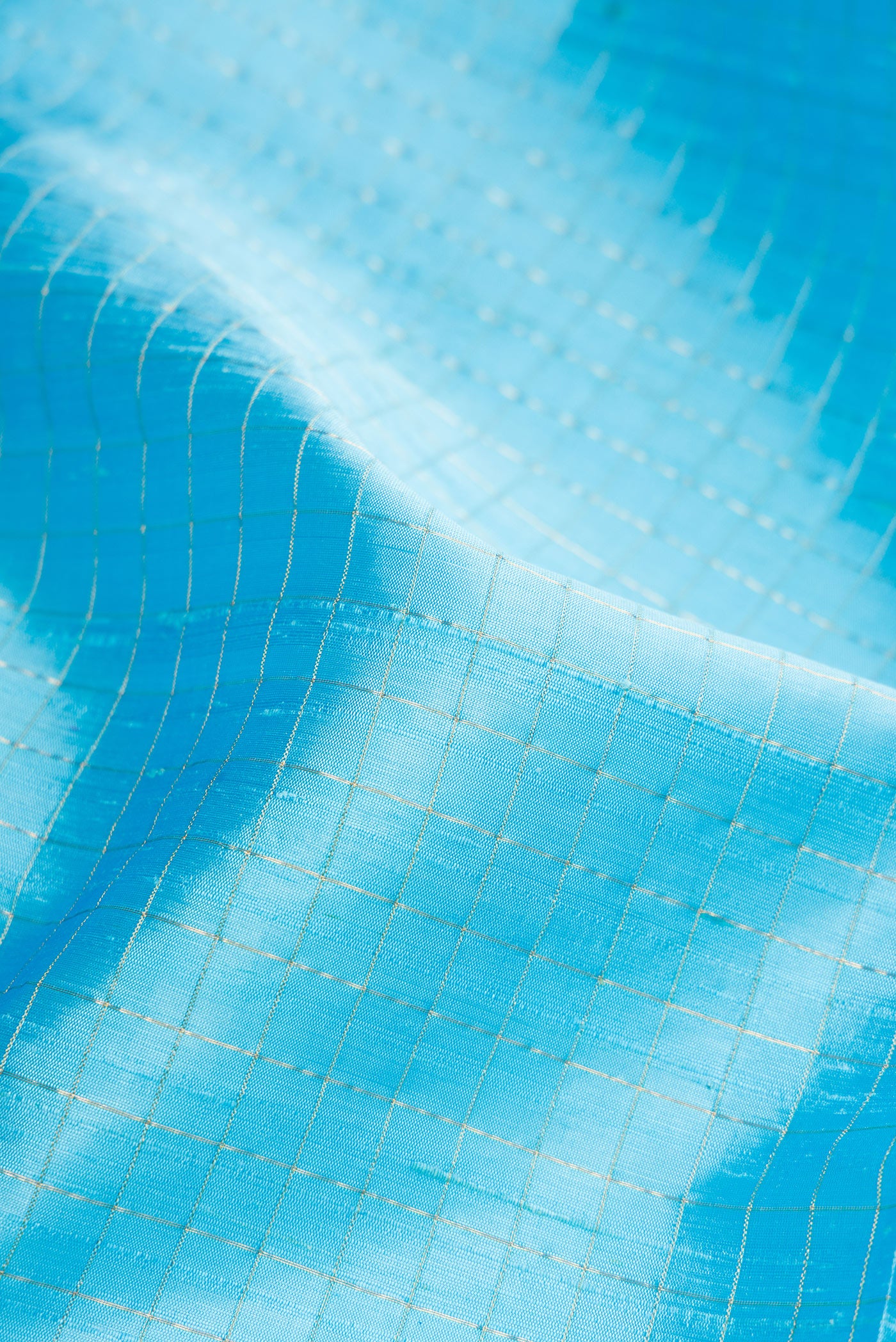 Close up of Sky Blue Raw Silk Saree with Checked design on the body and Zari Border.  displaying folds