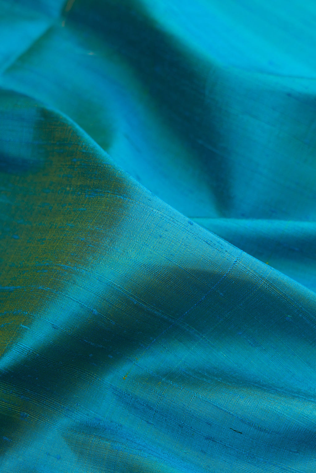 Close up of Peacock Blue Dual Tone Raw Silk Saree with Plain Body and Temple Border.  displaying folds
