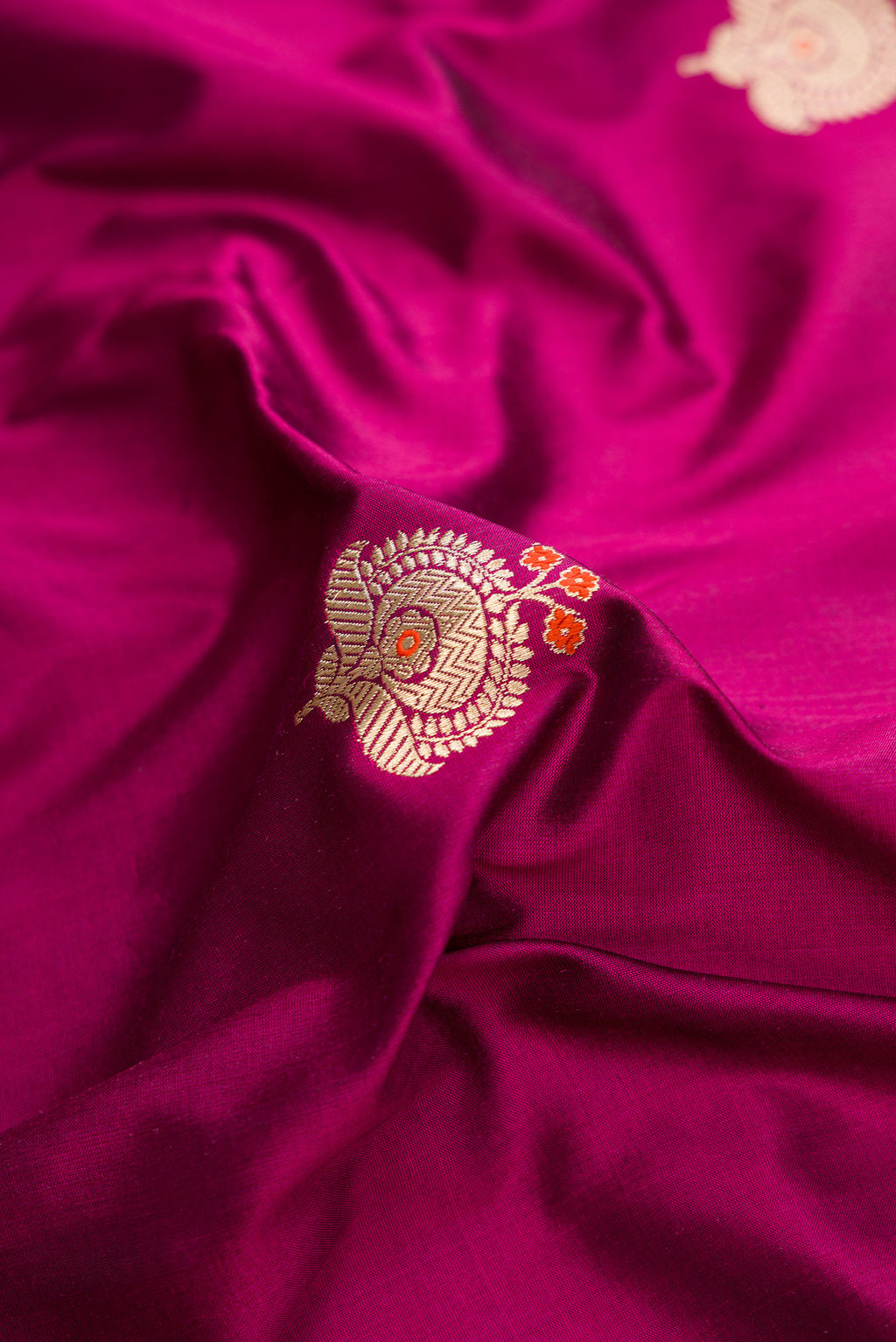 Close up of Magenta Dual Tone Banarasi Silk Saree with Zari And Thread Butta on the body and Fancy Border.  displaying folds