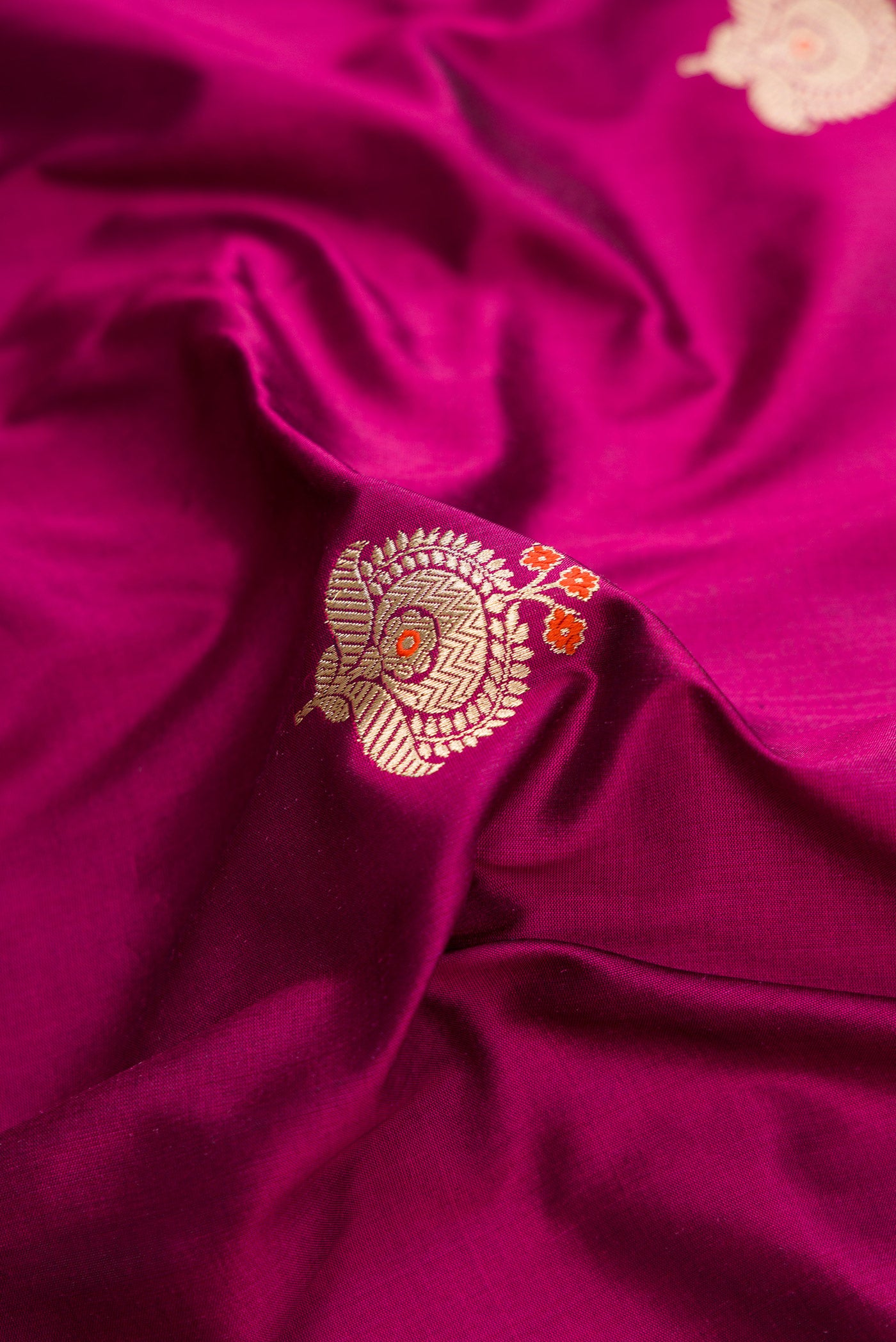 Close up of Magenta Dual Tone Banarasi Silk Saree with Zari And Thread Butta on the body and Fancy Border.  displaying folds