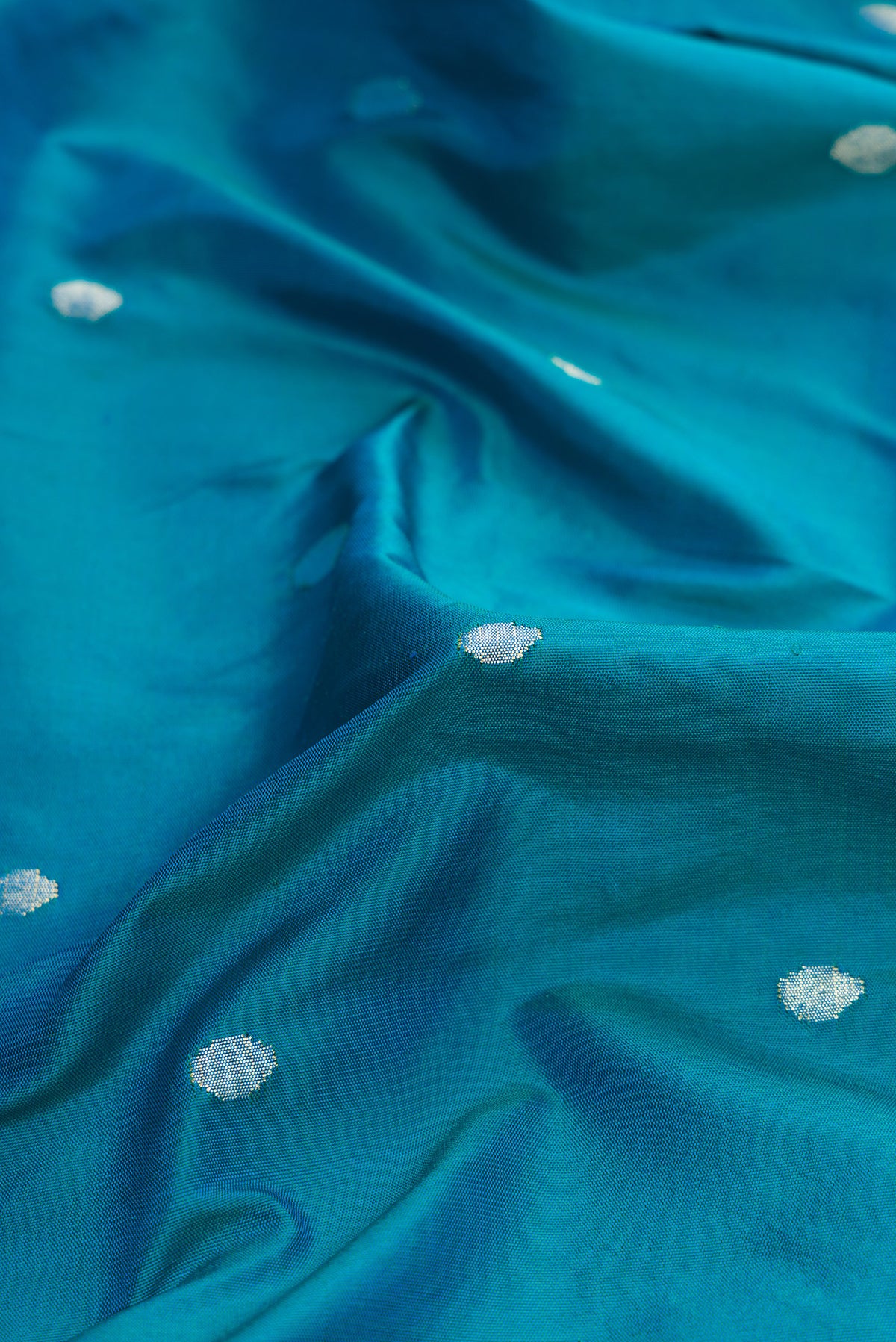 Close up of Pure Silk Pure Zari Peacock Blue Dual Tone Paithani Saree with Zari Butta on the body and Paithani Border.  displaying folds