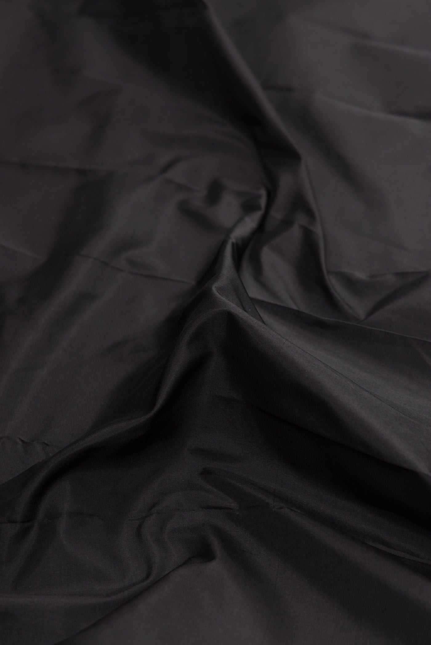 Close up of Black Dual Tone Kanjivaram Silk Saree with Plain Body and Zari Border.  displaying folds