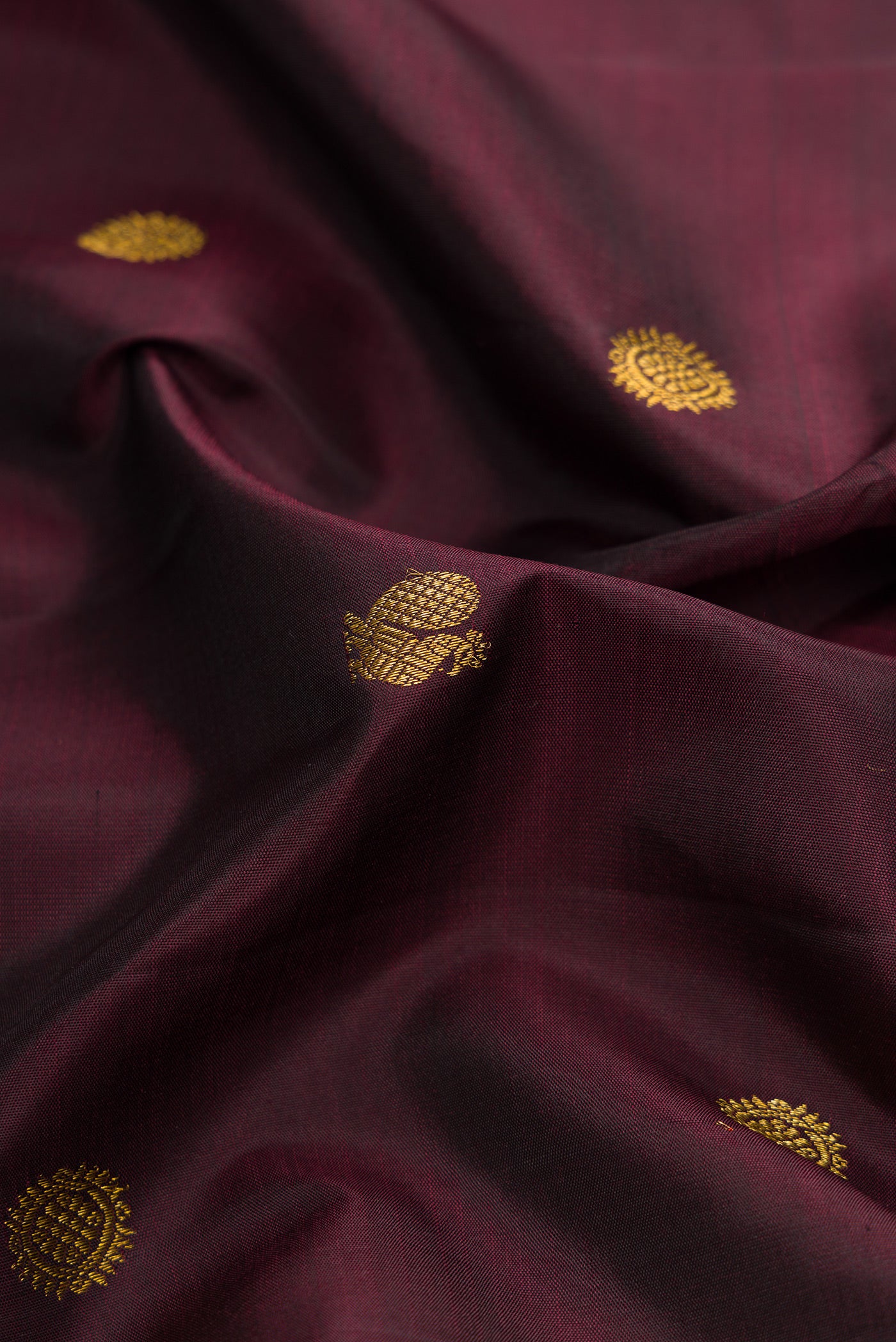 Close up of Burgundy Dual Tone Kanjivaram Silk Saree with Zari Butta on the body and Zari Border.  displaying folds