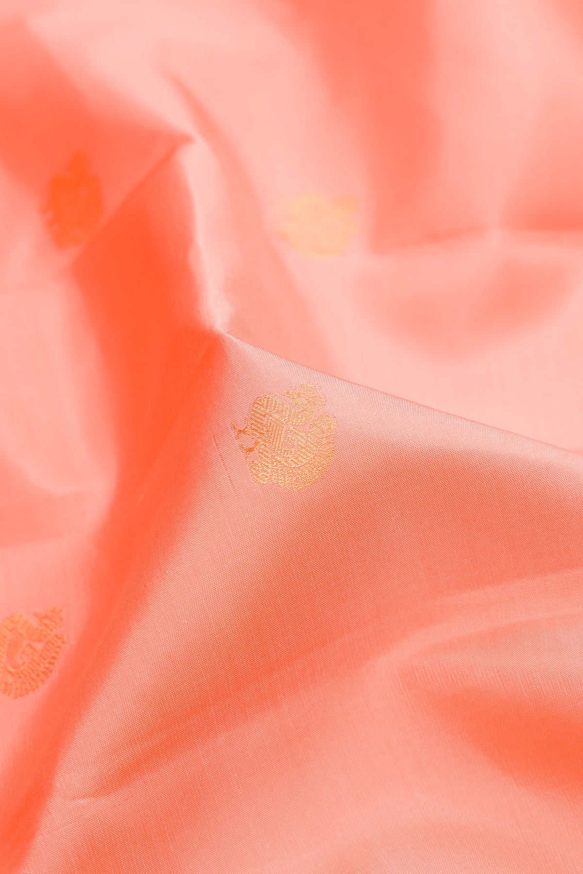 Close up of Peach Kanchipuram Silk Saree with Zari Butta on the body and Zari Border.  displaying folds