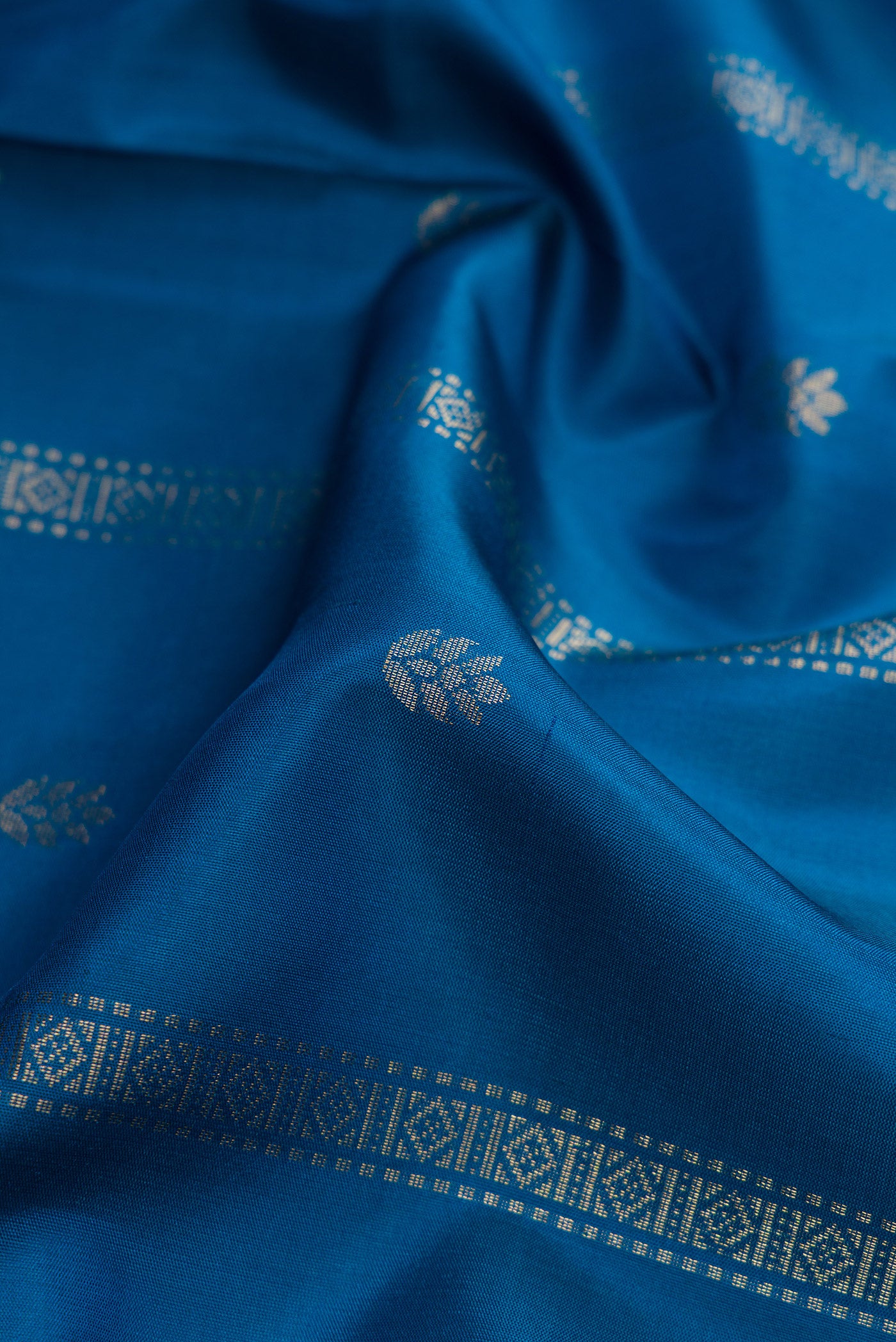 Close up of Peacock Blue Dual Tone Soft Silk Saree with Zari Butta on the body and Zari Border.  displaying folds