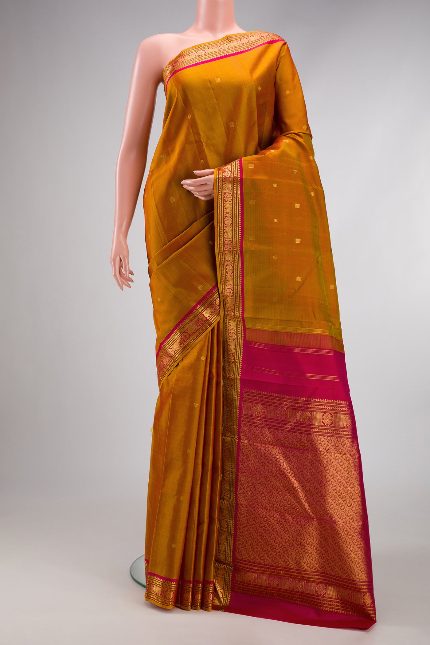 Mustard Kanjivaram Silk Saree with Zari Butta on the body and Zari Border.  displayed on a mannequin