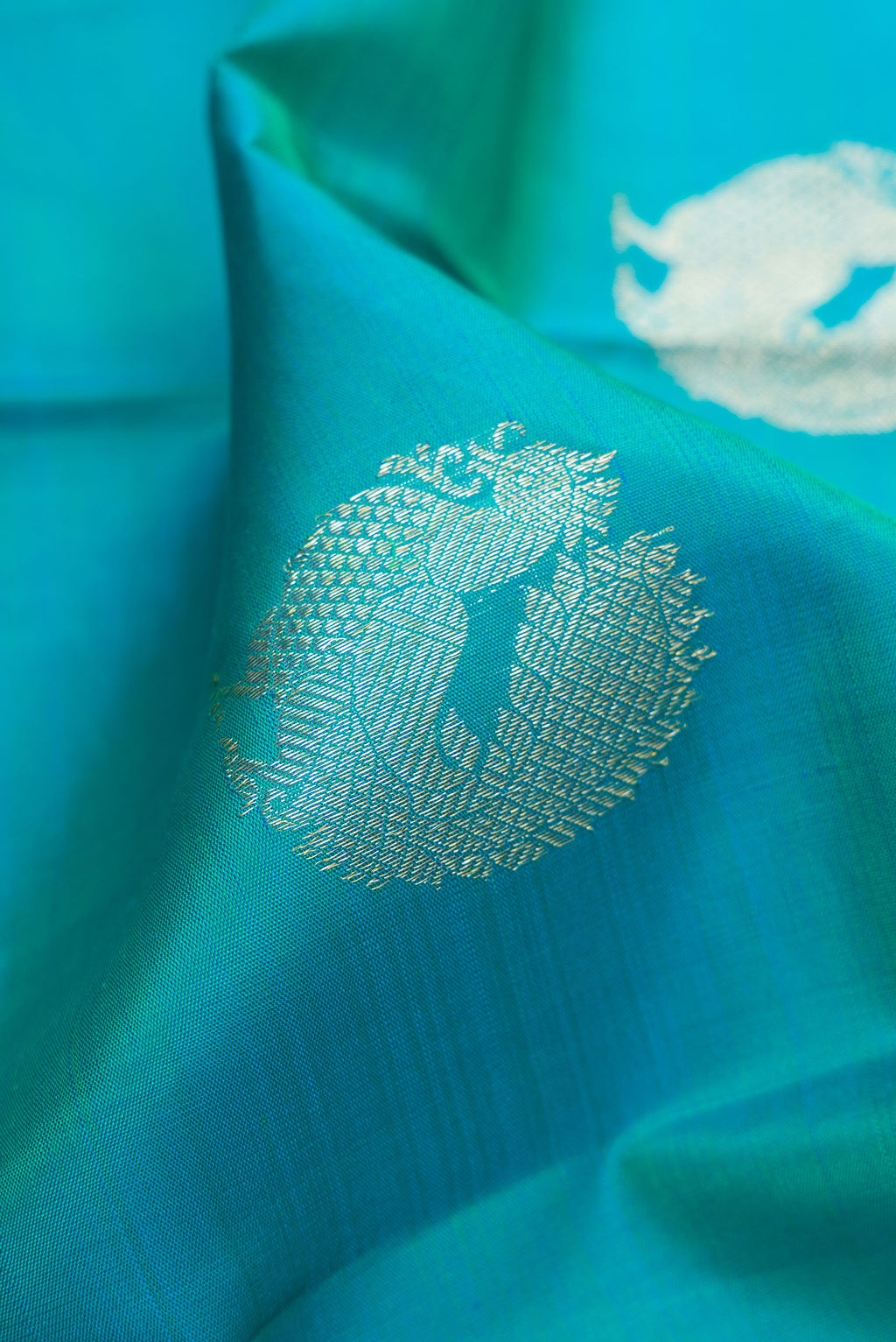 Close up of Peacock Blue Dual Tone Kanjivaram Silk Saree with Zari Butta on the body and Zari Border.  displaying folds