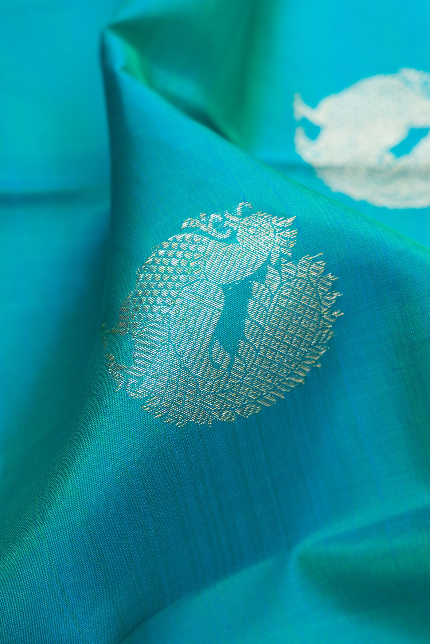 Close up of Peacock Blue Dual Tone Kanjivaram Silk Saree with Zari Butta on the body and Zari Border.  displaying folds