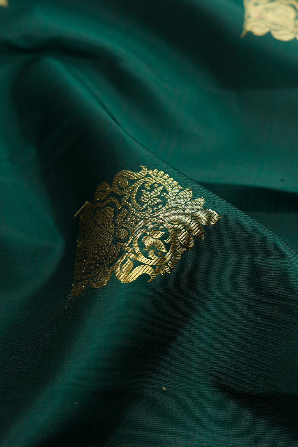 Close up of Bottle Green Kanjivaram Silk Saree with Zari Butta on the body and Zari Border.  displaying folds