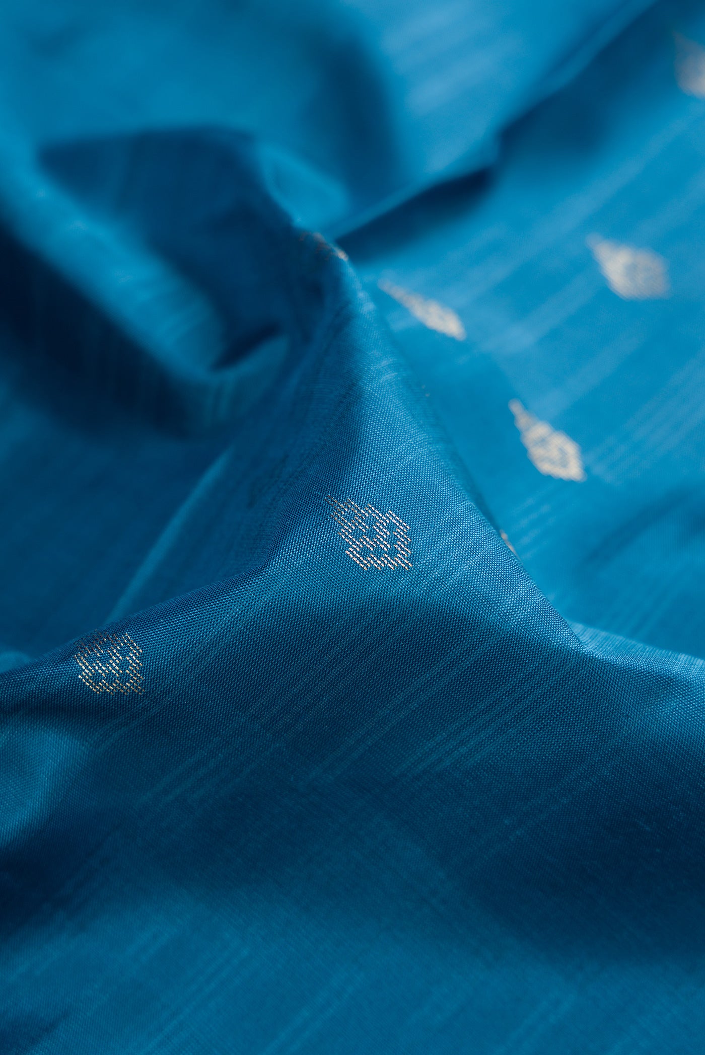 Close up of Peacock Blue Dual Tone Soft Silk Saree with Zari Butta on the body and Zari Border.  displaying folds