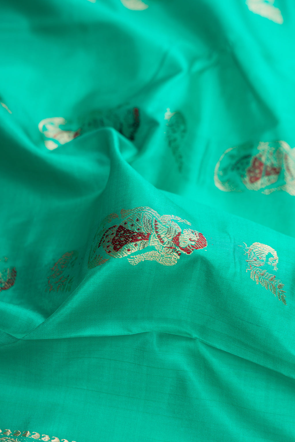 Close up of Sea Green Dual Tone Baluchari Silk Saree with Zari And Thread Butta on the body and Fancy Border.  displaying folds
