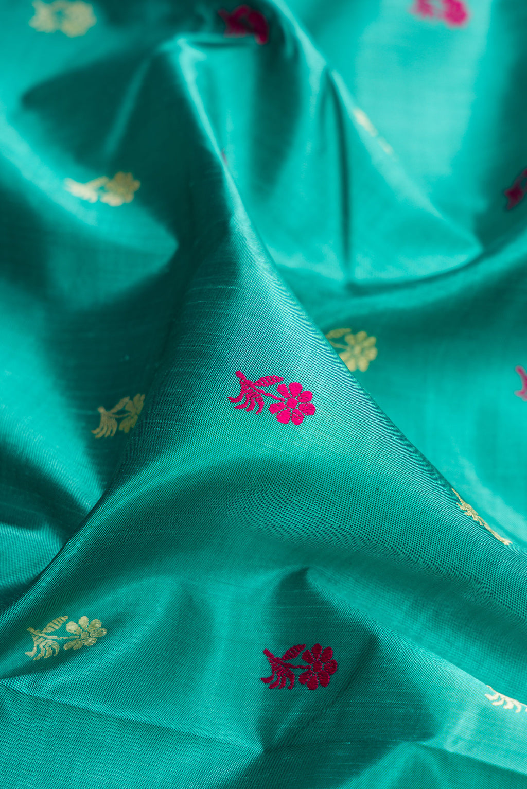 Close up of Turquoise Baluchari Silk Saree with Thread Butta on the body and Thread Border.  displaying folds