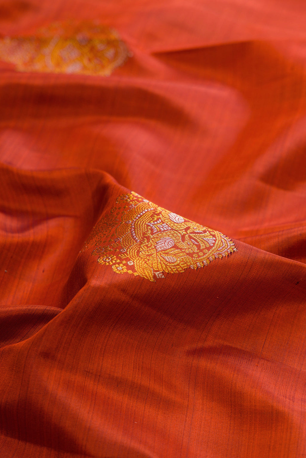 Close up of Pure Silk Rust Kanjivaram Saree with Zari Butta on the body and Zari Border.  displaying folds