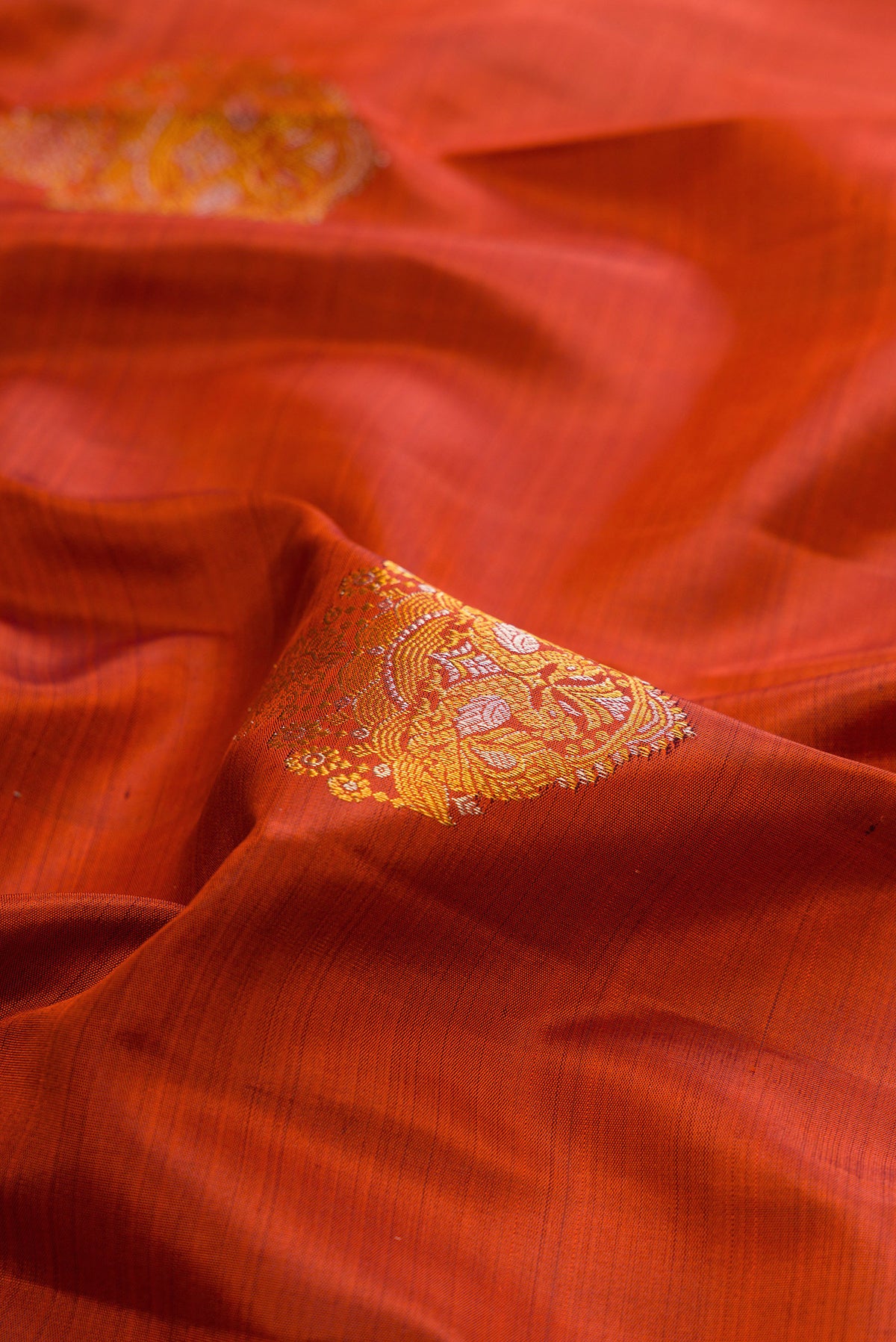 Close up of Pure Silk Rust Kanjivaram Saree with Zari Butta on the body and Zari Border.  displaying folds