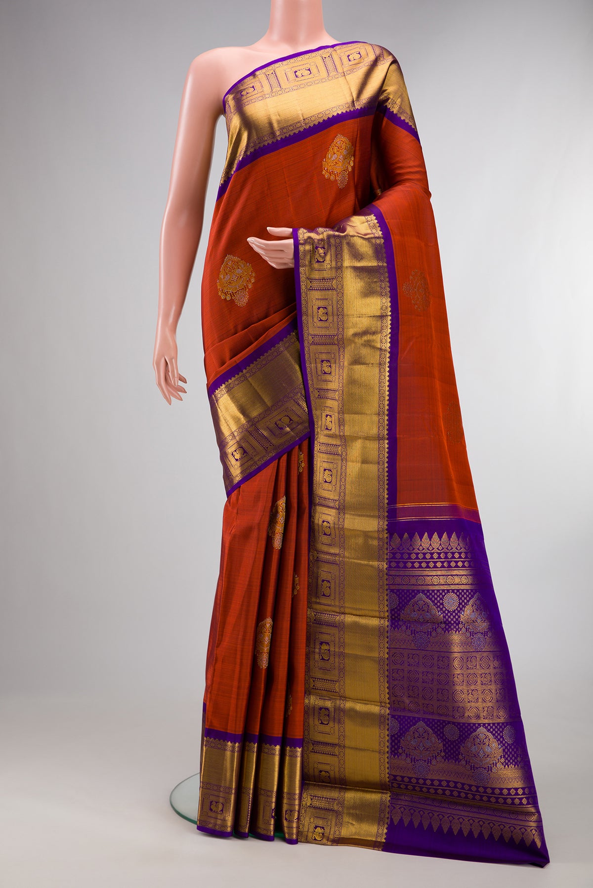 Pure Silk Rust Kanjivaram Saree with Zari Butta on the body and Zari Border.  displayed on a mannequin