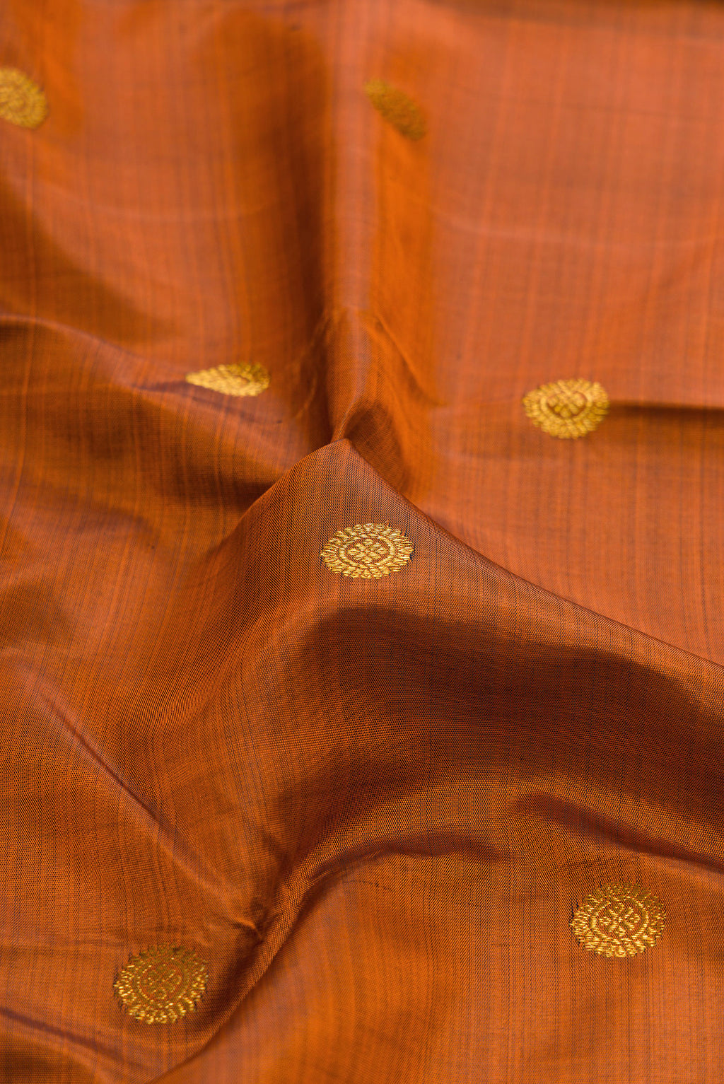 Close up of Rust Kanjivaram Silk Saree with Zari Butta on the body and Zari Border.  displaying folds