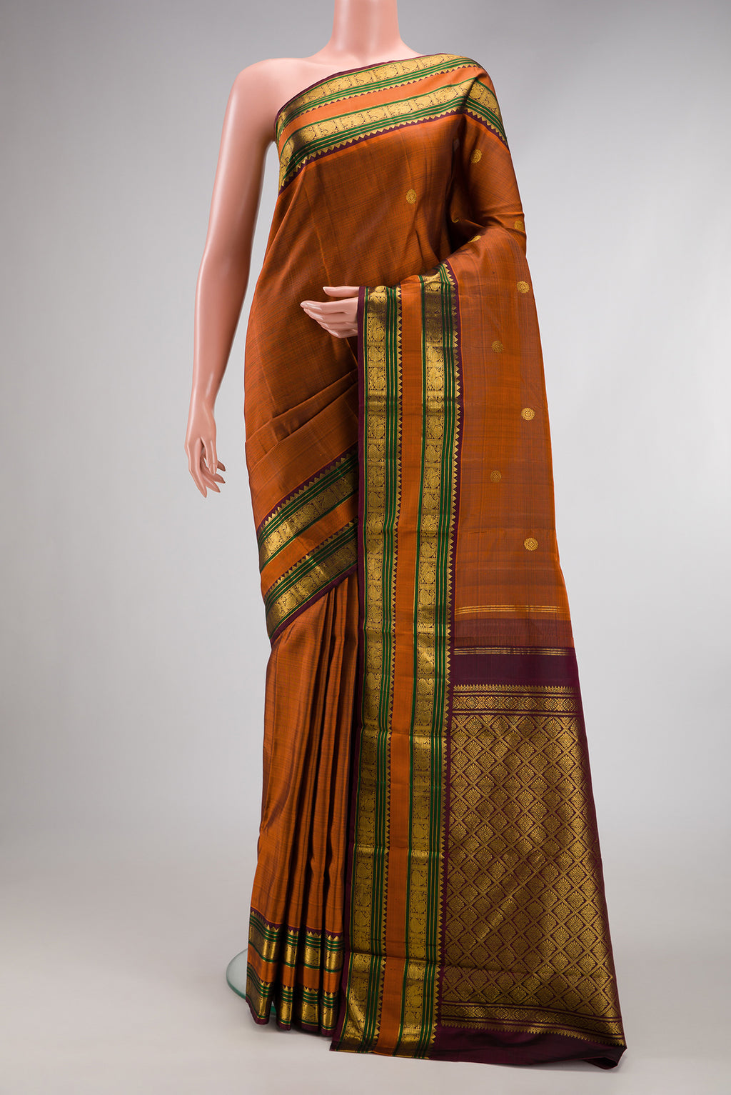 Rust Kanjivaram Silk Saree with Zari Butta on the body and Zari Border.  displayed on a mannequin