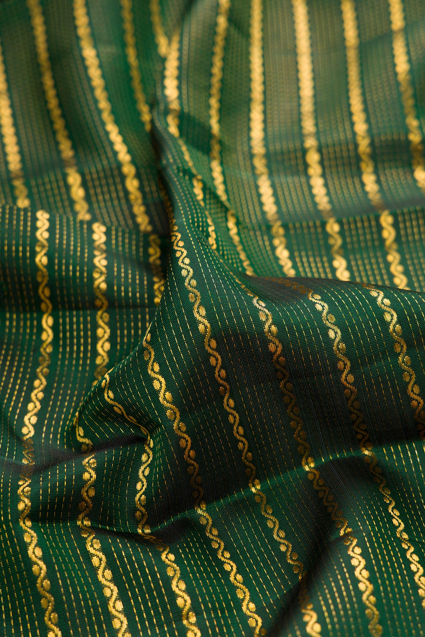 Close up of Bottle Green Kanchipuram Silk Saree with Veldhari on the body and Zari Border.  displaying folds