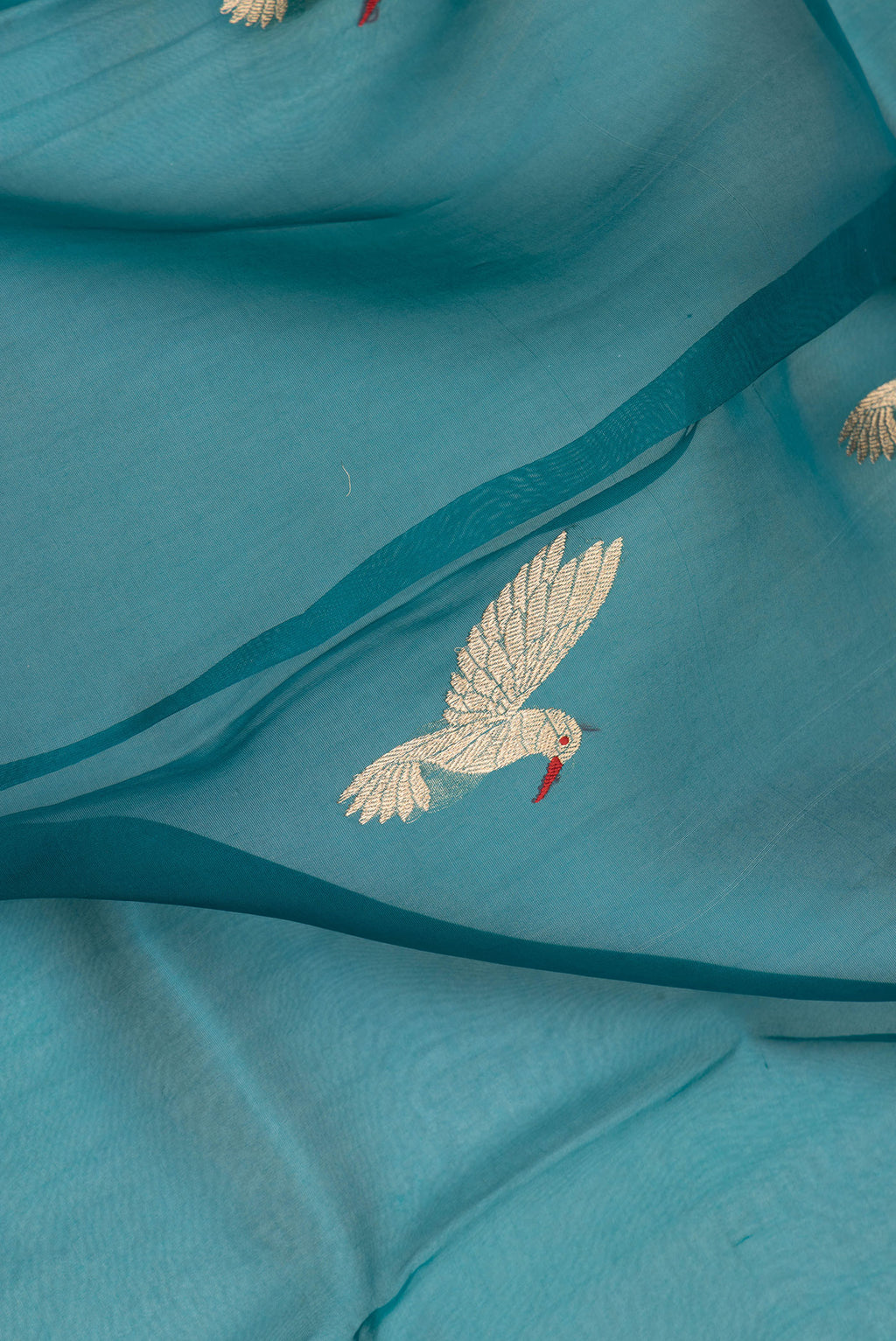 Close up of Peacock Blue Organza Saree with Zari Butta on the body and Zari Border.  displaying folds
