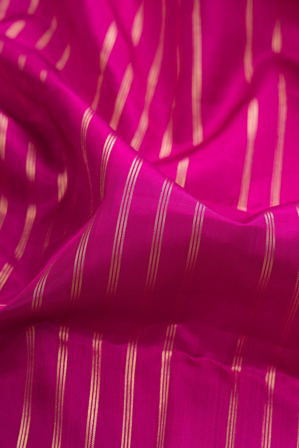 Close up of Pure Silk Rani Pink Kanchipuram Saree with Stripes on the body and Zari Border.  displaying folds