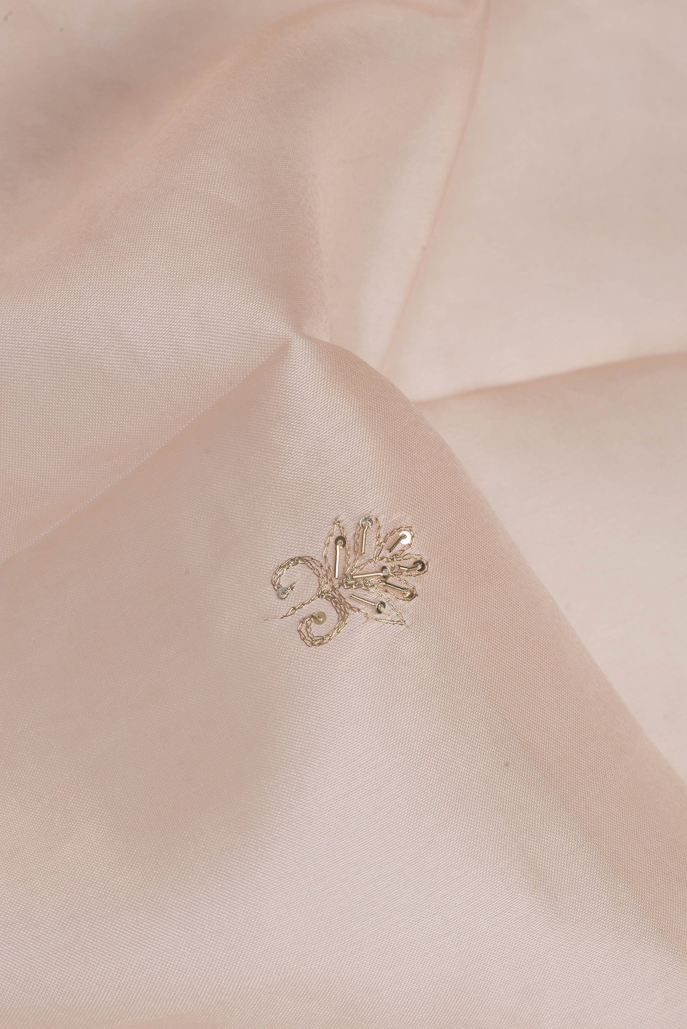 Close up of Rose Gold Organza Silk Saree with Embroidery on the body and Sequin Border.  displaying folds