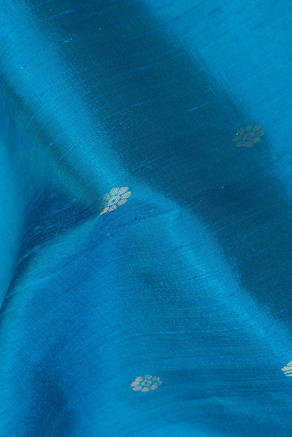 Close up of Light Blue Raw Saree with Zari Butta on the body and Zari Border.  displaying folds