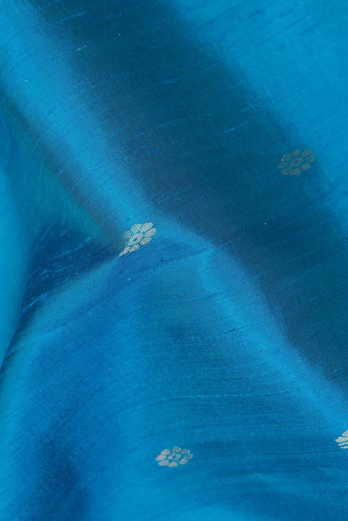 Close up of Light Blue Raw Saree with Zari Butta on the body and Zari Border.  displaying folds