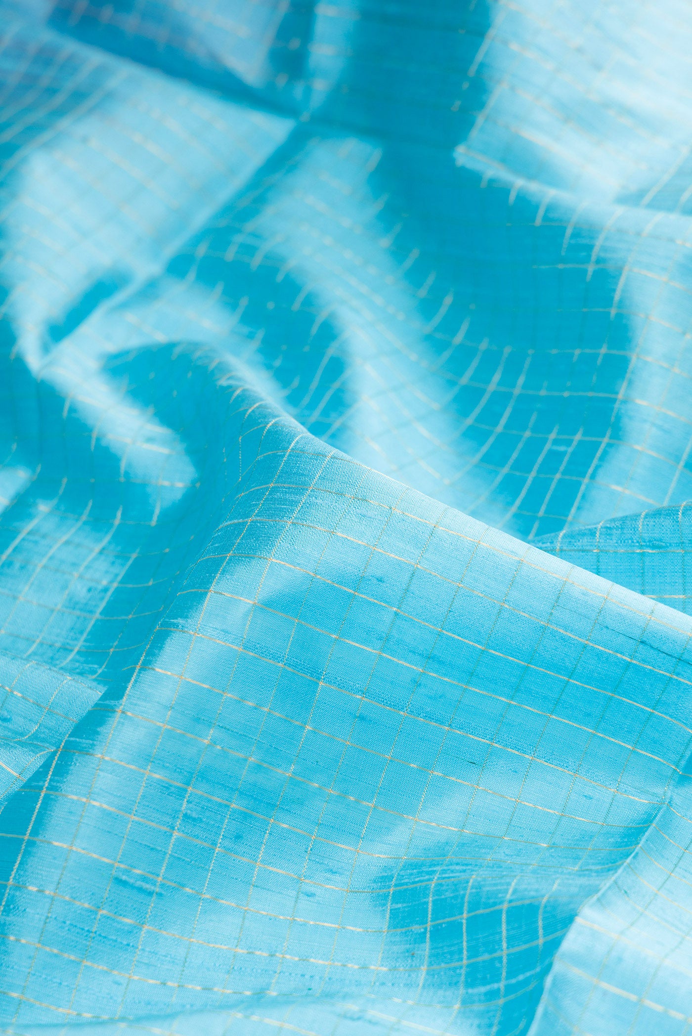 Close up of Pure Silk Sky Blue Raw Saree with Checked design on the body and Zari Border.  displaying folds