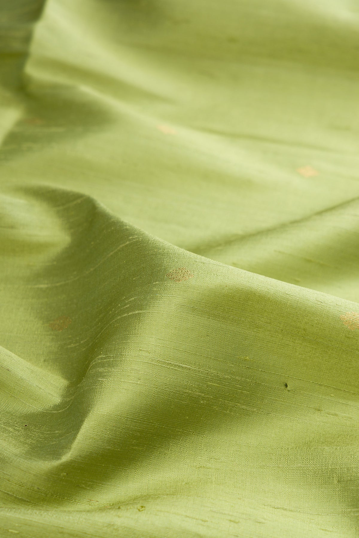 Close up of Pure Silk Pista Green Raw Saree with Zari Butta on the body and Zari Border.  displaying folds
