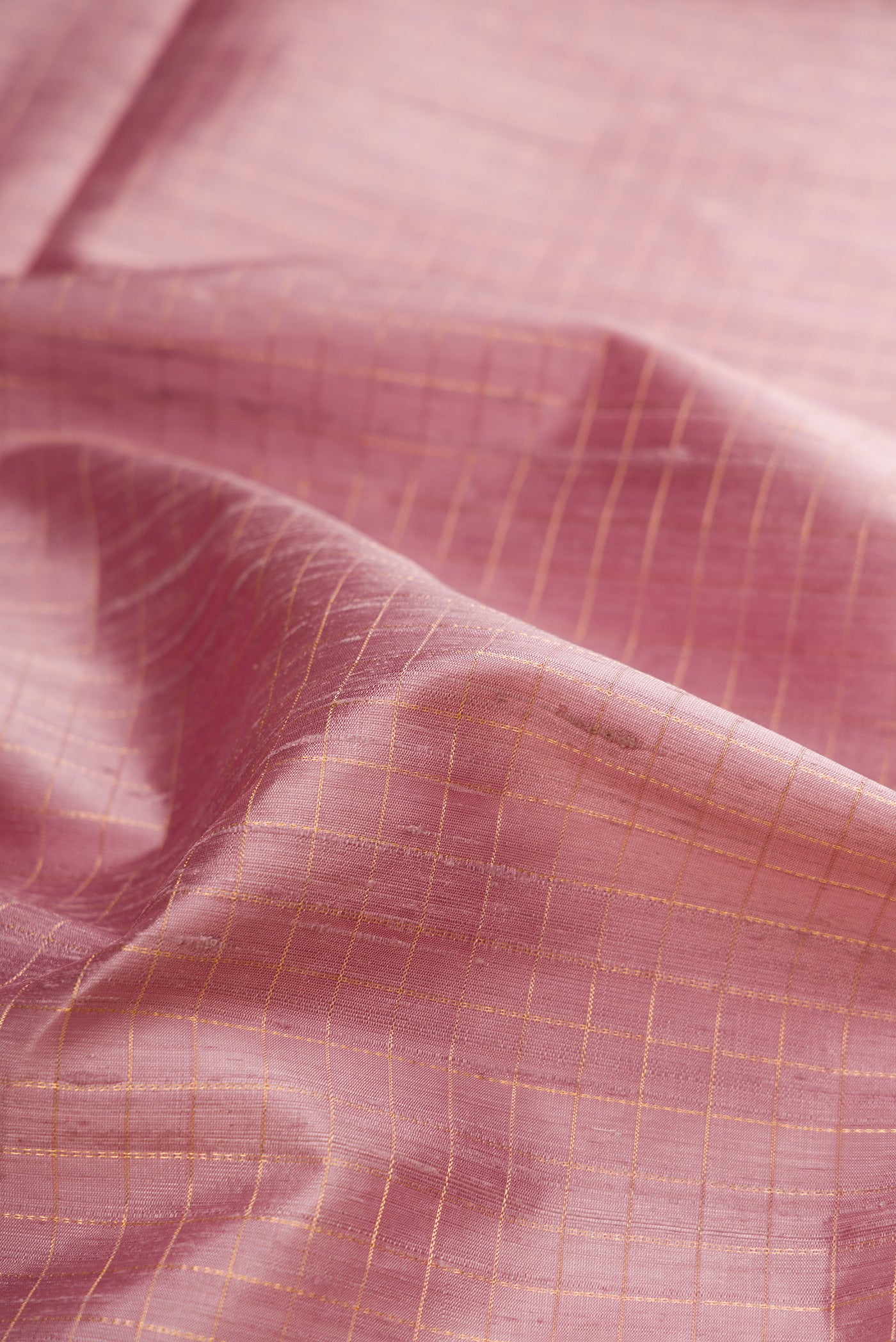 Close up of Pure Silk Rose Gold Raw Saree with Checked design on the body and Fancy Border.  displaying folds
