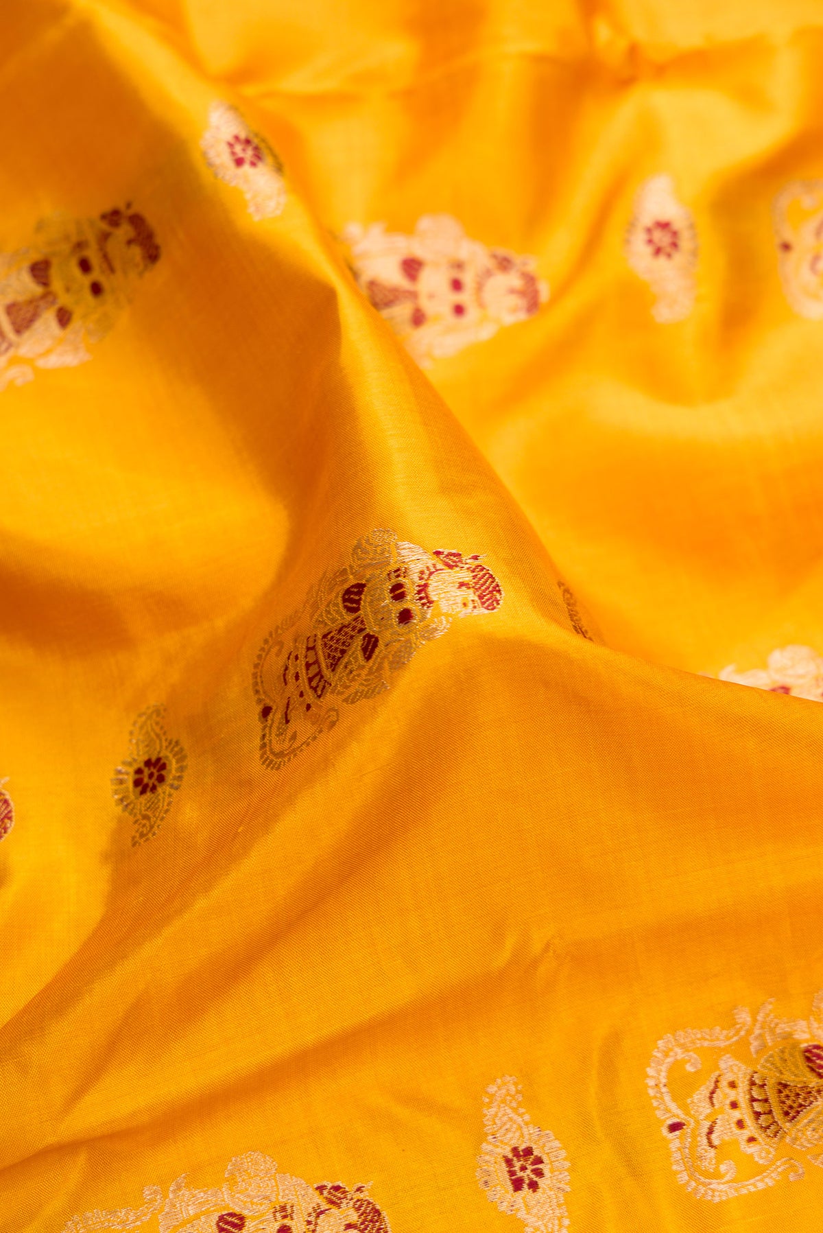 Close up of Pure Silk Mustard Baluchari Saree with Zari And Thread Butta on the body and Fancy Border.  displaying folds