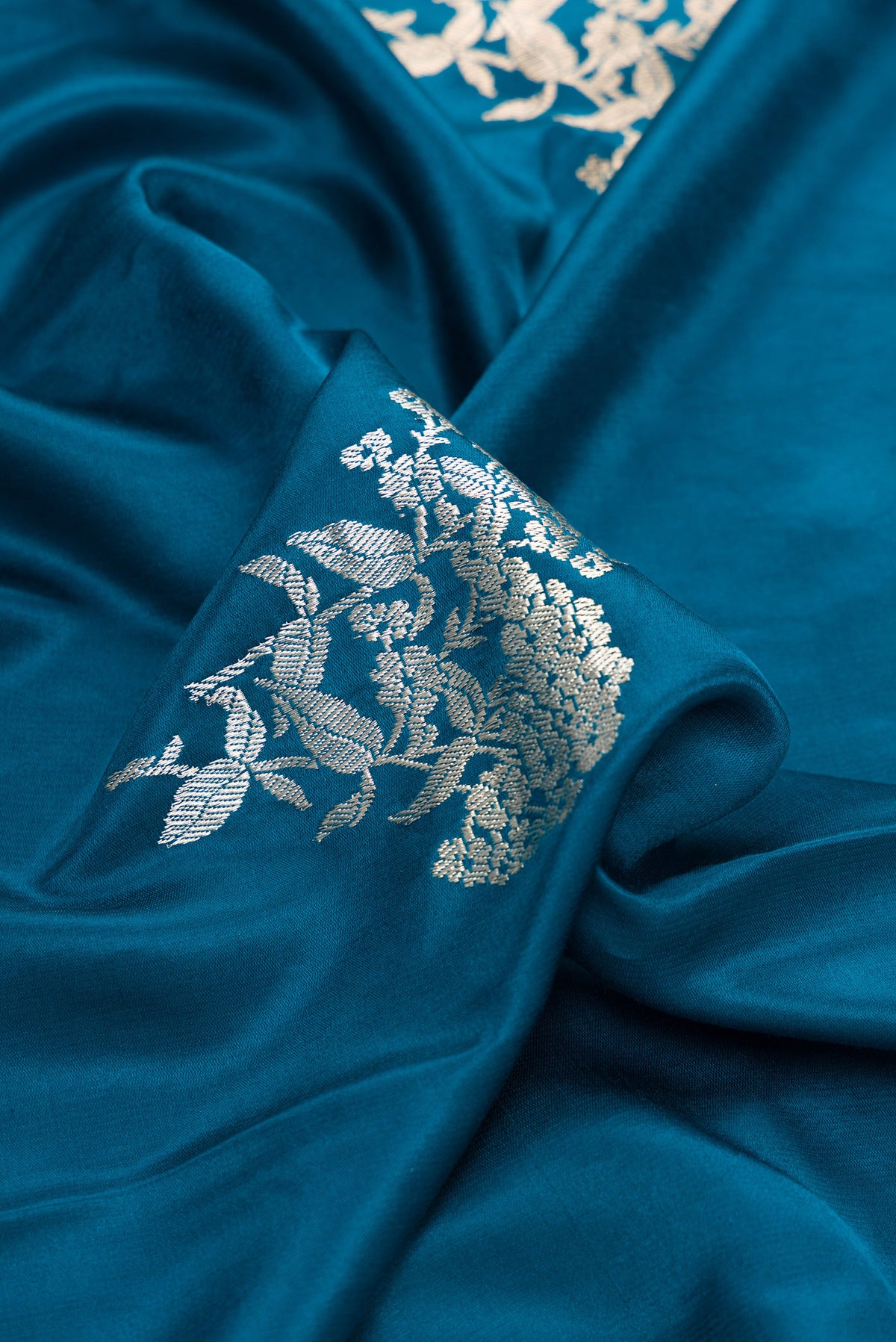 Close up of Pure Silk Peacock Blue Dual Tone Banarasi Saree with Zari Butta on the body and Zari Border.  displaying folds