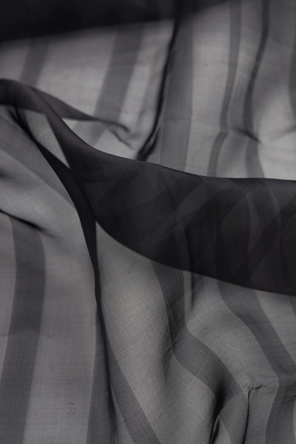 Close up of Black Organza Saree with Stripes on the body and Fancy Border.  displaying folds