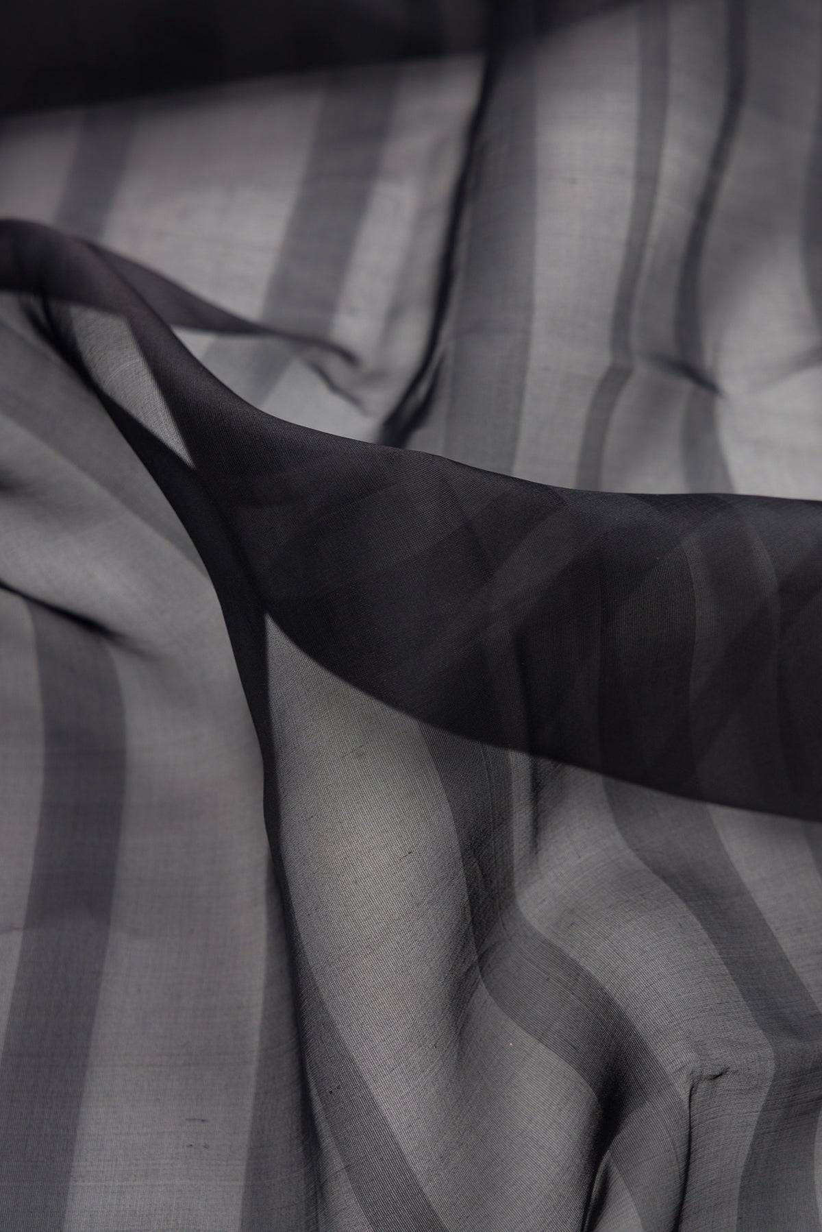 Close up of Black Organza Saree with Stripes on the body and Fancy Border.  displaying folds